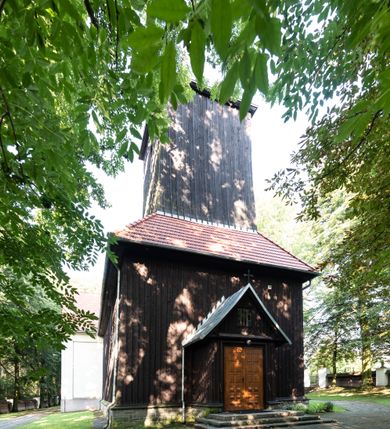 Zdjęcie nr 17: Kościół, otoczony starodrzewiem, położony jest na niewielkim wzniesieniu ponad stawami w centrum wsi. Jest to budowla drewniano-murowana, orientowana. Nawa została wzniesiona w 1518 roku na zrąb na rzucie zbliżonym do kwadratu, nakryta płaskim stropem. Od zachodu do nawy przylega wzniesiona w tym samym roku wieża o konstrukcji słupowej, pierwotnie kwadratowa o pochyłych ścianach, w 1782 roku poszerzona przez obudowanie drugą konstrukcją, prawie pionową. Wieża, w całości szalowana, poprzedzona niewielką kruchtą, w połowie wysokości jest opasana daszkiem pulpitowym. Jej hełm posiada kształt kopuły zwieńczonej ostrosłupem. Od południa do nawy przylega drewniana kruchta z 1924 roku, a od wschodu murowane prezbiterium z 1931 roku. Prezbiterium otwiera się podwójnymi arkadami na dwie kaplice boczne - wzniesioną od południa w 1861 roku z kryptą grobową Duninów oraz kaplicę przylegającą od północy zbudowaną w 1931 roku. Jego przestrzeń nakryto sklepieniem kolebkowym na gurtach, zaś dwuprzęsłowe kaplice sklepieniem krzyżowym. Za prezbiterium wznosi się murowana, piętrowa zakrystia z XVII wieku przykryta sklepieniem nieckowym z lunetami i małym zwierciadłem, zdobionym monogramem maryjnym. Jednokalenicowy dach nawy i prezbiterium pokryty jest dachówką. Nad końcu dachu nawy od wschodu nadwieszono wieżyczkę na sygnaturkę z latarnią i cebulastą banią, zwieńczoną krzyżem. Zakrystia nakryta została namiotowym dachem polskim, także pokrytym dachówką. Na zewnętrznych ścianach części murowanej umieszczono kilka epitafiów przeniesionych z wnętrza kościoła. Wewnątrz prezbiterium na ścianie wschodniej, nad wejściem do zakrystii, zawieszono manierystyczny, dwukondygnacyjny ołtarz główny z XVII wieku z uszakami zdobionymi herbami Starykoń i Jelita. Przy ścianie północnej, w miejscu połączenia nawy drewnianej z murowanym prezbiterium, usytuowano w 1931 roku ambonę oraz kamienną chrzcielnicę z 1658 roku. Belkę tęczową zdobi osiemnastowieczna grupa Ukrzyżowania. W kaplicach bocznych ustawiono dwa neobarokowe ołtarze boczne.  