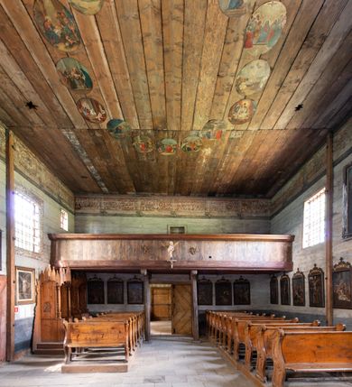 Zdjęcie nr 10: Kościół jest usytuowany ustronnie na stoku wzniesienia, otoczony starodrzewiem i parkanem, ujmującym stary cmentarz z nielicznymi mogiłami i nagrobkami. Orientowaną świątynię w całości wzniesiono z drewna. Zastosowano konstrukcję zrębową na murowanej podwalinie z murowaną kryptą pod prezbiterium. Nawa kościoła jest prawie kwadratowa. Od wchodu przylega do niej węższe prezbiterium zamknięte trójbocznie. Przy jego północnej ścianie wzniesiono bezokienną zakrystię z wejściem od strony wschodniej. Od zachodu z nawą łączy się wieża na rzucie kwadratu wzniesiona na tzw. słup. Ma pochyłe ściany, szalowane w dolnej części deskami, a w górnej podbite gontem. Wieża zakończona jest nadwieszoną izbicą, zwieńczoną ostrosłupowym hełmem gontowym. W połowie wysokości wieżę opasa pulpitowy daszek gontowy łączący się po bokach z dachem nawy. Pod wieżą urządzono obszerną kruchtę. Wysokie i spadziste dachy kościoła pokryte są gontem. Więźba ma konstrukcję storczykową. Ponad wschodnim szczytem nawy usytuowano nadwieszoną wieżyczkę na sygnaturkę o kształcie cebulastym z latarnią zwieńczoną krzyżem. Całość bryły kościoła (z wyjątkiem wieży) obiegają otwarte soboty, w które przed zakrystią od wschodu wbudowano nowy przedsionek. W nawie od południa znajduje się profilowany portal z nadprożem wykrojonym w ośli grzbiet. Umieszczone w nim drzwi zostały zaopatrzone w stare okucia i antabę. Wnętrze nawy i prezbiterium nakryto płaskimi stropami z pozostałościami późnorenesansowych malowideł z motywem kasetonów z rozetami. Łuk tęczowy jest ostry. Spływa na profilowaną belkę, która jest wsparta na kroksztynach. Na belce tęczowej został ustawiony krucyfiks oraz figury Matki Boskiej i św. Jana Apostoła. Chór muzyczny z dekorowanym malarsko parapetem został wsparty na dwóch słupach. W świątyni znajduje się rokokowy ołtarz główny z obrazem ze sceną Zwiastowania NMP. Dwa ołtarze boczne ustawione zostały przy łuku tęczowym. Prawy ołtarz boczny św. Karola Boromeusza pochodzi z drugiej połowy XVII wieku. Na to miejsce trafił on w połowie XX wieku z kaplicy pałacu w Osieku. Lewy ołtarz boczny jest późnobarokowy z około 1700 roku. W jego centrum umieszczono obraz Matki Boskiej Piekarskiej. Na północnej ścianie nad wejściem do zakrystii zawieszono epitafium Mikołaja i Beaty z Mirowa Porębskich z 1611 roku. Wcześniej epitafium pełniło rolę retabulum w miejscu stojącego dziś ołtarza św. Karola Boromeusza. W prezbiterium przy łuku tęczowym zawieszono rokokową ambonę w kształcie łodzi, na którą wejście prowadzi z zakrystii. Przy wejściu do nawy znajduje się kamienna chrzcielnica z początku XVI wieku, ozdobiona herbem Fogelweder, z drewnianą, późnobarokową nakrywą. W zakrystii zachował się także rokokowy drewniany lawetarz z drugiej połowy XVIII wieku.     