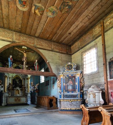 Zdjęcie nr 8: Kościół jest usytuowany ustronnie na stoku wzniesienia, otoczony starodrzewiem i parkanem, ujmującym stary cmentarz z nielicznymi mogiłami i nagrobkami. Orientowaną świątynię w całości wzniesiono z drewna. Zastosowano konstrukcję zrębową na murowanej podwalinie z murowaną kryptą pod prezbiterium. Nawa kościoła jest prawie kwadratowa. Od wchodu przylega do niej węższe prezbiterium zamknięte trójbocznie. Przy jego północnej ścianie wzniesiono bezokienną zakrystię z wejściem od strony wschodniej. Od zachodu z nawą łączy się wieża na rzucie kwadratu wzniesiona na tzw. słup. Ma pochyłe ściany, szalowane w dolnej części deskami, a w górnej podbite gontem. Wieża zakończona jest nadwieszoną izbicą, zwieńczoną ostrosłupowym hełmem gontowym. W połowie wysokości wieżę opasa pulpitowy daszek gontowy łączący się po bokach z dachem nawy. Pod wieżą urządzono obszerną kruchtę. Wysokie i spadziste dachy kościoła pokryte są gontem. Więźba ma konstrukcję storczykową. Ponad wschodnim szczytem nawy usytuowano nadwieszoną wieżyczkę na sygnaturkę o kształcie cebulastym z latarnią zwieńczoną krzyżem. Całość bryły kościoła (z wyjątkiem wieży) obiegają otwarte soboty, w które przed zakrystią od wschodu wbudowano nowy przedsionek. W nawie od południa znajduje się profilowany portal z nadprożem wykrojonym w ośli grzbiet. Umieszczone w nim drzwi zostały zaopatrzone w stare okucia i antabę. Wnętrze nawy i prezbiterium nakryto płaskimi stropami z pozostałościami późnorenesansowych malowideł z motywem kasetonów z rozetami. Łuk tęczowy jest ostry. Spływa na profilowaną belkę, która jest wsparta na kroksztynach. Na belce tęczowej został ustawiony krucyfiks oraz figury Matki Boskiej i św. Jana Apostoła. Chór muzyczny z dekorowanym malarsko parapetem został wsparty na dwóch słupach. W świątyni znajduje się rokokowy ołtarz główny z obrazem ze sceną Zwiastowania NMP. Dwa ołtarze boczne ustawione zostały przy łuku tęczowym. Prawy ołtarz boczny św. Karola Boromeusza pochodzi z drugiej połowy XVII wieku. Na to miejsce trafił on w połowie XX wieku z kaplicy pałacu w Osieku. Lewy ołtarz boczny jest późnobarokowy z około 1700 roku. W jego centrum umieszczono obraz Matki Boskiej Piekarskiej. Na północnej ścianie nad wejściem do zakrystii zawieszono epitafium Mikołaja i Beaty z Mirowa Porębskich z 1611 roku. Wcześniej epitafium pełniło rolę retabulum w miejscu stojącego dziś ołtarza św. Karola Boromeusza. W prezbiterium przy łuku tęczowym zawieszono rokokową ambonę w kształcie łodzi, na którą wejście prowadzi z zakrystii. Przy wejściu do nawy znajduje się kamienna chrzcielnica z początku XVI wieku, ozdobiona herbem Fogelweder, z drewnianą, późnobarokową nakrywą. W zakrystii zachował się także rokokowy drewniany lawetarz z drugiej połowy XVIII wieku.     