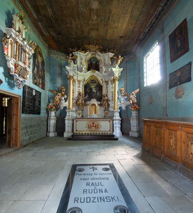 Zdjęcie nr 12: Kościół jest usytuowany ustronnie na stoku wzniesienia, otoczony starodrzewiem i parkanem, ujmującym stary cmentarz z nielicznymi mogiłami i nagrobkami. Orientowaną świątynię w całości wzniesiono z drewna. Zastosowano konstrukcję zrębową na murowanej podwalinie z murowaną kryptą pod prezbiterium. Nawa kościoła jest prawie kwadratowa. Od wchodu przylega do niej węższe prezbiterium zamknięte trójbocznie. Przy jego północnej ścianie wzniesiono bezokienną zakrystię z wejściem od strony wschodniej. Od zachodu z nawą łączy się wieża na rzucie kwadratu wzniesiona na tzw. słup. Ma pochyłe ściany, szalowane w dolnej części deskami, a w górnej podbite gontem. Wieża zakończona jest nadwieszoną izbicą, zwieńczoną ostrosłupowym hełmem gontowym. W połowie wysokości wieżę opasa pulpitowy daszek gontowy łączący się po bokach z dachem nawy. Pod wieżą urządzono obszerną kruchtę. Wysokie i spadziste dachy kościoła pokryte są gontem. Więźba ma konstrukcję storczykową. Ponad wschodnim szczytem nawy usytuowano nadwieszoną wieżyczkę na sygnaturkę o kształcie cebulastym z latarnią zwieńczoną krzyżem. Całość bryły kościoła (z wyjątkiem wieży) obiegają otwarte soboty, w które przed zakrystią od wschodu wbudowano nowy przedsionek. W nawie od południa znajduje się profilowany portal z nadprożem wykrojonym w ośli grzbiet. Umieszczone w nim drzwi zostały zaopatrzone w stare okucia i antabę. Wnętrze nawy i prezbiterium nakryto płaskimi stropami z pozostałościami późnorenesansowych malowideł z motywem kasetonów z rozetami. Łuk tęczowy jest ostry. Spływa na profilowaną belkę, która jest wsparta na kroksztynach. Na belce tęczowej został ustawiony krucyfiks oraz figury Matki Boskiej i św. Jana Apostoła. Chór muzyczny z dekorowanym malarsko parapetem został wsparty na dwóch słupach. W świątyni znajduje się rokokowy ołtarz główny z obrazem ze sceną Zwiastowania NMP. Dwa ołtarze boczne ustawione zostały przy łuku tęczowym. Prawy ołtarz boczny św. Karola Boromeusza pochodzi z drugiej połowy XVII wieku. Na to miejsce trafił on w połowie XX wieku z kaplicy pałacu w Osieku. Lewy ołtarz boczny jest późnobarokowy z około 1700 roku. W jego centrum umieszczono obraz Matki Boskiej Piekarskiej. Na północnej ścianie nad wejściem do zakrystii zawieszono epitafium Mikołaja i Beaty z Mirowa Porębskich z 1611 roku. Wcześniej epitafium pełniło rolę retabulum w miejscu stojącego dziś ołtarza św. Karola Boromeusza. W prezbiterium przy łuku tęczowym zawieszono rokokową ambonę w kształcie łodzi, na którą wejście prowadzi z zakrystii. Przy wejściu do nawy znajduje się kamienna chrzcielnica z początku XVI wieku, ozdobiona herbem Fogelweder, z drewnianą, późnobarokową nakrywą. W zakrystii zachował się także rokokowy drewniany lawetarz z drugiej połowy XVIII wieku.     