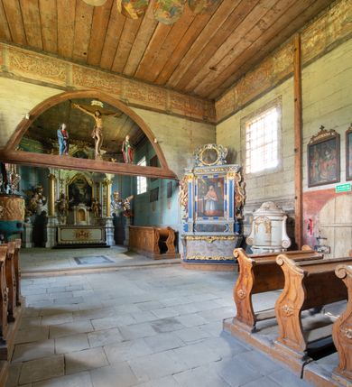 Zdjęcie nr 14: Kościół jest usytuowany ustronnie na stoku wzniesienia, otoczony starodrzewiem i parkanem, ujmującym stary cmentarz z nielicznymi mogiłami i nagrobkami. Orientowaną świątynię w całości wzniesiono z drewna. Zastosowano konstrukcję zrębową na murowanej podwalinie z murowaną kryptą pod prezbiterium. Nawa kościoła jest prawie kwadratowa. Od wchodu przylega do niej węższe prezbiterium zamknięte trójbocznie. Przy jego północnej ścianie wzniesiono bezokienną zakrystię z wejściem od strony wschodniej. Od zachodu z nawą łączy się wieża na rzucie kwadratu wzniesiona na tzw. słup. Ma pochyłe ściany, szalowane w dolnej części deskami, a w górnej podbite gontem. Wieża zakończona jest nadwieszoną izbicą, zwieńczoną ostrosłupowym hełmem gontowym. W połowie wysokości wieżę opasa pulpitowy daszek gontowy łączący się po bokach z dachem nawy. Pod wieżą urządzono obszerną kruchtę. Wysokie i spadziste dachy kościoła pokryte są gontem. Więźba ma konstrukcję storczykową. Ponad wschodnim szczytem nawy usytuowano nadwieszoną wieżyczkę na sygnaturkę o kształcie cebulastym z latarnią zwieńczoną krzyżem. Całość bryły kościoła (z wyjątkiem wieży) obiegają otwarte soboty, w które przed zakrystią od wschodu wbudowano nowy przedsionek. W nawie od południa znajduje się profilowany portal z nadprożem wykrojonym w ośli grzbiet. Umieszczone w nim drzwi zostały zaopatrzone w stare okucia i antabę. Wnętrze nawy i prezbiterium nakryto płaskimi stropami z pozostałościami późnorenesansowych malowideł z motywem kasetonów z rozetami. Łuk tęczowy jest ostry. Spływa na profilowaną belkę, która jest wsparta na kroksztynach. Na belce tęczowej został ustawiony krucyfiks oraz figury Matki Boskiej i św. Jana Apostoła. Chór muzyczny z dekorowanym malarsko parapetem został wsparty na dwóch słupach. W świątyni znajduje się rokokowy ołtarz główny z obrazem ze sceną Zwiastowania NMP. Dwa ołtarze boczne ustawione zostały przy łuku tęczowym. Prawy ołtarz boczny św. Karola Boromeusza pochodzi z drugiej połowy XVII wieku. Na to miejsce trafił on w połowie XX wieku z kaplicy pałacu w Osieku. Lewy ołtarz boczny jest późnobarokowy z około 1700 roku. W jego centrum umieszczono obraz Matki Boskiej Piekarskiej. Na północnej ścianie nad wejściem do zakrystii zawieszono epitafium Mikołaja i Beaty z Mirowa Porębskich z 1611 roku. Wcześniej epitafium pełniło rolę retabulum w miejscu stojącego dziś ołtarza św. Karola Boromeusza. W prezbiterium przy łuku tęczowym zawieszono rokokową ambonę w kształcie łodzi, na którą wejście prowadzi z zakrystii. Przy wejściu do nawy znajduje się kamienna chrzcielnica z początku XVI wieku, ozdobiona herbem Fogelweder, z drewnianą, późnobarokową nakrywą. W zakrystii zachował się także rokokowy drewniany lawetarz z drugiej połowy XVIII wieku.     