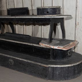 Zdjęcie nr 1: Malowany na czarno katafalk z listwami dekorowanymi białą farbą składa się z kilku części. Jego podstawę tworzą dwa zmniejszające się stopnie na rzucie wydłużonego prostokąta o półkoliście zamkniętych, nadwieszonych krótszych bokach. Dłuższe boki dolnego stopnia i krótsze boki górnego stopnia zdobi malowane na biało wyobrażenie stylizowanej trupiej czaszki. Na górnym stopniu ustawiono ławę malowaną na czarno, wspartą na wyciętych falisto w desce czterech nogach z białym blatem na rzucie wydłużonego prostokąta o półokrągłych krótszych bokach. Na blacie znajdują się dwie półokrągłe czarne podstawy pod trumnę, dekorowane od przodu malowaną na biało stylizowaną trupią czaszką i skrzyżowanymi piszczelami. 