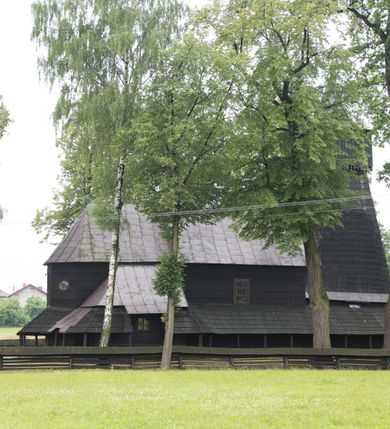 Zdjęcie nr 7: Drewnianą architekturę kościoła charakteryzuje konstrukcja zrębowa. Bryłę świątyni tworzy korpus nawowy oraz węższe, zakończone trójbocznie prezbiterium z przylegającą od północy zakrystią. Od zachodu do korpusu dostawiono wieżę o konstrukcji słupowo-ramowej z izbicą, zwieńczoną cebulastym hełmem przechodzącym w ostrosłup. Ściany pokryte są gontem, izbica wieży pionowym szalunkiem z listwowaniem, dekoracyjnym wycięciem oraz okrągłymi otworami. Korpus nawowy i prezbiterium nakrywają oddzielne, wielopołaciowe dachy o zróżnicowanej wysokości kalenicy, kryte blachą. Wokół bryły kościoła znajdują się otwarte soboty z wydatnymi dachami gontowymi. 
Wnętrze świątyni przekrywają płaskie stropy wydzielone profilowanym gzymsem. Otwory drzwiowe ujęte są późnogotyckimi portalami o nadprożach w formie tzw. łuku w ośli grzbiet. Profilowany łuk tęczowy ma kształt półokrągły i jest nadwieszony na kroksztynach. Ściany i stropy pokryte są polichromią.       
