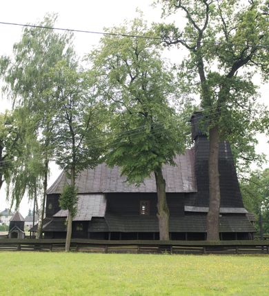 Zdjęcie nr 6: Drewnianą architekturę kościoła charakteryzuje konstrukcja zrębowa. Bryłę świątyni tworzy korpus nawowy oraz węższe, zakończone trójbocznie prezbiterium z przylegającą od północy zakrystią. Od zachodu do korpusu dostawiono wieżę o konstrukcji słupowo-ramowej z izbicą, zwieńczoną cebulastym hełmem przechodzącym w ostrosłup. Ściany pokryte są gontem, izbica wieży pionowym szalunkiem z listwowaniem, dekoracyjnym wycięciem oraz okrągłymi otworami. Korpus nawowy i prezbiterium nakrywają oddzielne, wielopołaciowe dachy o zróżnicowanej wysokości kalenicy, kryte blachą. Wokół bryły kościoła znajdują się otwarte soboty z wydatnymi dachami gontowymi. 
Wnętrze świątyni przekrywają płaskie stropy wydzielone profilowanym gzymsem. Otwory drzwiowe ujęte są późnogotyckimi portalami o nadprożach w formie tzw. łuku w ośli grzbiet. Profilowany łuk tęczowy ma kształt półokrągły i jest nadwieszony na kroksztynach. Ściany i stropy pokryte są polichromią.       
