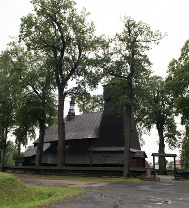 Zdjęcie nr 5: Drewnianą architekturę kościoła charakteryzuje konstrukcja zrębowa. Bryłę świątyni tworzy korpus nawowy oraz węższe, zakończone trójbocznie prezbiterium z przylegającą od północy zakrystią. Od zachodu do korpusu dostawiono wieżę o konstrukcji słupowo-ramowej z izbicą, zwieńczoną cebulastym hełmem przechodzącym w ostrosłup. Ściany pokryte są gontem, izbica wieży pionowym szalunkiem z listwowaniem, dekoracyjnym wycięciem oraz okrągłymi otworami. Korpus nawowy i prezbiterium nakrywają oddzielne, wielopołaciowe dachy o zróżnicowanej wysokości kalenicy, kryte blachą. Wokół bryły kościoła znajdują się otwarte soboty z wydatnymi dachami gontowymi. 
Wnętrze świątyni przekrywają płaskie stropy wydzielone profilowanym gzymsem. Otwory drzwiowe ujęte są późnogotyckimi portalami o nadprożach w formie tzw. łuku w ośli grzbiet. Profilowany łuk tęczowy ma kształt półokrągły i jest nadwieszony na kroksztynach. Ściany i stropy pokryte są polichromią.       

