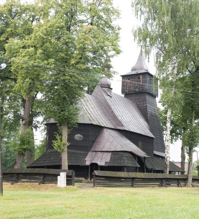 Zdjęcie nr 8: Drewnianą architekturę kościoła charakteryzuje konstrukcja zrębowa. Bryłę świątyni tworzy korpus nawowy oraz węższe, zakończone trójbocznie prezbiterium z przylegającą od północy zakrystią. Od zachodu do korpusu dostawiono wieżę o konstrukcji słupowo-ramowej z izbicą, zwieńczoną cebulastym hełmem przechodzącym w ostrosłup. Ściany pokryte są gontem, izbica wieży pionowym szalunkiem z listwowaniem, dekoracyjnym wycięciem oraz okrągłymi otworami. Korpus nawowy i prezbiterium nakrywają oddzielne, wielopołaciowe dachy o zróżnicowanej wysokości kalenicy, kryte blachą. Wokół bryły kościoła znajdują się otwarte soboty z wydatnymi dachami gontowymi. 
Wnętrze świątyni przekrywają płaskie stropy wydzielone profilowanym gzymsem. Otwory drzwiowe ujęte są późnogotyckimi portalami o nadprożach w formie tzw. łuku w ośli grzbiet. Profilowany łuk tęczowy ma kształt półokrągły i jest nadwieszony na kroksztynach. Ściany i stropy pokryte są polichromią.       
