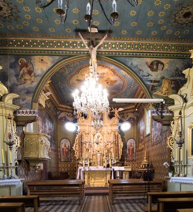 Zdjęcie nr 9: Drewnianą architekturę kościoła charakteryzuje konstrukcja zrębowa. Bryłę świątyni tworzy korpus nawowy oraz węższe, zakończone trójbocznie prezbiterium z przylegającą od północy zakrystią. Od zachodu do korpusu dostawiono wieżę o konstrukcji słupowo-ramowej z izbicą, zwieńczoną cebulastym hełmem przechodzącym w ostrosłup. Ściany pokryte są gontem, izbica wieży pionowym szalunkiem z listwowaniem, dekoracyjnym wycięciem oraz okrągłymi otworami. Korpus nawowy i prezbiterium nakrywają oddzielne, wielopołaciowe dachy o zróżnicowanej wysokości kalenicy, kryte blachą. Wokół bryły kościoła znajdują się otwarte soboty z wydatnymi dachami gontowymi. 
Wnętrze świątyni przekrywają płaskie stropy wydzielone profilowanym gzymsem. Otwory drzwiowe ujęte są późnogotyckimi portalami o nadprożach w formie tzw. łuku w ośli grzbiet. Profilowany łuk tęczowy ma kształt półokrągły i jest nadwieszony na kroksztynach. Ściany i stropy pokryte są polichromią.       
