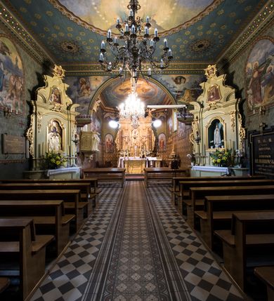 Zdjęcie nr 12: Drewnianą architekturę kościoła charakteryzuje konstrukcja zrębowa. Bryłę świątyni tworzy korpus nawowy oraz węższe, zakończone trójbocznie prezbiterium z przylegającą od północy zakrystią. Od zachodu do korpusu dostawiono wieżę o konstrukcji słupowo-ramowej z izbicą, zwieńczoną cebulastym hełmem przechodzącym w ostrosłup. Ściany pokryte są gontem, izbica wieży pionowym szalunkiem z listwowaniem, dekoracyjnym wycięciem oraz okrągłymi otworami. Korpus nawowy i prezbiterium nakrywają oddzielne, wielopołaciowe dachy o zróżnicowanej wysokości kalenicy, kryte blachą. Wokół bryły kościoła znajdują się otwarte soboty z wydatnymi dachami gontowymi. 
Wnętrze świątyni przekrywają płaskie stropy wydzielone profilowanym gzymsem. Otwory drzwiowe ujęte są późnogotyckimi portalami o nadprożach w formie tzw. łuku w ośli grzbiet. Profilowany łuk tęczowy ma kształt półokrągły i jest nadwieszony na kroksztynach. Ściany i stropy pokryte są polichromią.       
