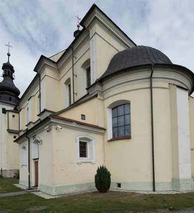 Zdjęcie nr 16: Kościół jest położony w centrum wsi, na wschód od głównej drogi, na placu otoczonym kamiennym murem przykrytym dachówką, z kilkoma drzewami. Wejście na plac przykościelny prowadzi przez szerokie schody i bramę od zachodu i bramkę od północy. Kościół jest budowlą założoną na planie prostokąta, jednonawowy, trójprzęsłowy z węższym, dwuprzęsłowym prezbiterium z apsydą. Do nawy przylegają od zachodu i północy dwie kruchty na planie kwadratu i wieża w narożu południowo-zachodnim fasady. Do prezbiterium od północy jest dostawiona kaplica na rzucie prostokąta otwierająca się półkolistymi arkadami, a od południa zakrystia. 
Artykulacja ścian jest przeprowadzona za pomocą zdwojonych pilastrów toskańskich stojących na wysokich postumentach i podtrzymujących wydatne, przełamujące się, pełne belkowanie z fryzem tryglifowym oraz wysuniętym gzymsem, obiegającym całe wnętrze świątyni. Wnętrze nakrywa sklepienie kolebkowe na gurtach z lunetami; w kluczach sklepienia znajdują się tarcze herbowe, Złota Pilawa oraz Ostoja. W lunetach umieszczone są okna prostokątne zamknięte łukiem odcinkowym; takie same okna znajdują się w apsydzie prezbiterium, poniżej belkowania.  W kaplicy znajdują się dwa prostokątne okna zamknięte odcinkowo. Zakrystia jest jednoprzestrzenna, nakryta sklepieniem krzyżowym. Prowadzi do niej kamienny portal profilowany z uszakami, z podwieszonymi wolutami, zwieńczony wydatnym gzymsem. W partii fryzu umieszczono polichromowany kartusz z herbem Ostoja. W ścianach środkowego przęsła korpusu nawowego po obu stronach kościoła znajdują się głębokie, prostokątne nisze zamknięte łukami odcinkowymi. W niszy północnej umieszczono drzwi prowadzące do niewielkiej kruchty przykrytej stropem, z dwoma małymi, okrągłymi oknami po bokach. Również po zachodniej stronie korpusu znajduje się wejście do kruchty. Ponadto na ścianach nawy oraz prezbiterium widnieją płyciny ujęte ramą profilowaną w tynku. W pierwszym od strony fasady przęśle znajduje się murowany chór muzyczny, trójarkadowy, wsparty na dwóch filarach opiętych pilastrami oraz dwóch półfilarach przylegających do ścian, sklepiony krzyżowo. 
Fasada kościoła jest płaska, zakończona gzymsem, z czterokondygnacyjną wieżą, nakrytą cebulastym hełmem z krzyżem. Boczne elewacje ujęte uskokowymi przyporami, zakończone gzymsem. Dachy dwuspadowe nad nawą i kruchtami, trójspadowe nad prezbiterium, półsferyczne nad apsydą, pulpitowe nad kaplicą i zakrystią, kryte blachą. Nad granicy nawy i prezbiterium wieloboczna wieżyczka na sygnaturkę z prześwitami, zakończona kopułą, sterczyną i kulą z krzyżem. 
