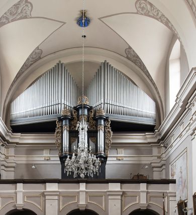 Zdjęcie nr 21: Kościół jest położony w centrum wsi, na wschód od głównej drogi, na placu otoczonym kamiennym murem przykrytym dachówką, z kilkoma drzewami. Wejście na plac przykościelny prowadzi przez szerokie schody i bramę od zachodu i bramkę od północy. Kościół jest budowlą założoną na planie prostokąta, jednonawowy, trójprzęsłowy z węższym, dwuprzęsłowym prezbiterium z apsydą. Do nawy przylegają od zachodu i północy dwie kruchty na planie kwadratu i wieża w narożu południowo-zachodnim fasady. Do prezbiterium od północy jest dostawiona kaplica na rzucie prostokąta otwierająca się półkolistymi arkadami, a od południa zakrystia. 
Artykulacja ścian jest przeprowadzona za pomocą zdwojonych pilastrów toskańskich stojących na wysokich postumentach i podtrzymujących wydatne, przełamujące się, pełne belkowanie z fryzem tryglifowym oraz wysuniętym gzymsem, obiegającym całe wnętrze świątyni. Wnętrze nakrywa sklepienie kolebkowe na gurtach z lunetami; w kluczach sklepienia znajdują się tarcze herbowe, Złota Pilawa oraz Ostoja. W lunetach umieszczone są okna prostokątne zamknięte łukiem odcinkowym; takie same okna znajdują się w apsydzie prezbiterium, poniżej belkowania.  W kaplicy znajdują się dwa prostokątne okna zamknięte odcinkowo. Zakrystia jest jednoprzestrzenna, nakryta sklepieniem krzyżowym. Prowadzi do niej kamienny portal profilowany z uszakami, z podwieszonymi wolutami, zwieńczony wydatnym gzymsem. W partii fryzu umieszczono polichromowany kartusz z herbem Ostoja. W ścianach środkowego przęsła korpusu nawowego po obu stronach kościoła znajdują się głębokie, prostokątne nisze zamknięte łukami odcinkowymi. W niszy północnej umieszczono drzwi prowadzące do niewielkiej kruchty przykrytej stropem, z dwoma małymi, okrągłymi oknami po bokach. Również po zachodniej stronie korpusu znajduje się wejście do kruchty. Ponadto na ścianach nawy oraz prezbiterium widnieją płyciny ujęte ramą profilowaną w tynku. W pierwszym od strony fasady przęśle znajduje się murowany chór muzyczny, trójarkadowy, wsparty na dwóch filarach opiętych pilastrami oraz dwóch półfilarach przylegających do ścian, sklepiony krzyżowo. 
Fasada kościoła jest płaska, zakończona gzymsem, z czterokondygnacyjną wieżą, nakrytą cebulastym hełmem z krzyżem. Boczne elewacje ujęte uskokowymi przyporami, zakończone gzymsem. Dachy dwuspadowe nad nawą i kruchtami, trójspadowe nad prezbiterium, półsferyczne nad apsydą, pulpitowe nad kaplicą i zakrystią, kryte blachą. Nad granicy nawy i prezbiterium wieloboczna wieżyczka na sygnaturkę z prześwitami, zakończona kopułą, sterczyną i kulą z krzyżem. 
