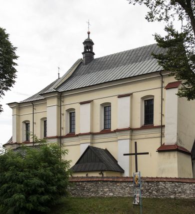 Zdjęcie nr 1: Kościół jest położony w centrum wsi, na wschód od głównej drogi, na placu otoczonym kamiennym murem przykrytym dachówką, z kilkoma drzewami. Wejście na plac przykościelny prowadzi przez szerokie schody i bramę od zachodu i bramkę od północy. Kościół jest budowlą założoną na planie prostokąta, jednonawowy, trójprzęsłowy z węższym, dwuprzęsłowym prezbiterium z apsydą. Do nawy przylegają od zachodu i północy dwie kruchty na planie kwadratu i wieża w narożu południowo-zachodnim fasady. Do prezbiterium od północy jest dostawiona kaplica na rzucie prostokąta otwierająca się półkolistymi arkadami, a od południa zakrystia. 
Artykulacja ścian jest przeprowadzona za pomocą zdwojonych pilastrów toskańskich stojących na wysokich postumentach i podtrzymujących wydatne, przełamujące się, pełne belkowanie z fryzem tryglifowym oraz wysuniętym gzymsem, obiegającym całe wnętrze świątyni. Wnętrze nakrywa sklepienie kolebkowe na gurtach z lunetami; w kluczach sklepienia znajdują się tarcze herbowe, Złota Pilawa oraz Ostoja. W lunetach umieszczone są okna prostokątne zamknięte łukiem odcinkowym; takie same okna znajdują się w apsydzie prezbiterium, poniżej belkowania.  W kaplicy znajdują się dwa prostokątne okna zamknięte odcinkowo. Zakrystia jest jednoprzestrzenna, nakryta sklepieniem krzyżowym. Prowadzi do niej kamienny portal profilowany z uszakami, z podwieszonymi wolutami, zwieńczony wydatnym gzymsem. W partii fryzu umieszczono polichromowany kartusz z herbem Ostoja. W ścianach środkowego przęsła korpusu nawowego po obu stronach kościoła znajdują się głębokie, prostokątne nisze zamknięte łukami odcinkowymi. W niszy północnej umieszczono drzwi prowadzące do niewielkiej kruchty przykrytej stropem, z dwoma małymi, okrągłymi oknami po bokach. Również po zachodniej stronie korpusu znajduje się wejście do kruchty. Ponadto na ścianach nawy oraz prezbiterium widnieją płyciny ujęte ramą profilowaną w tynku. W pierwszym od strony fasady przęśle znajduje się murowany chór muzyczny, trójarkadowy, wsparty na dwóch filarach opiętych pilastrami oraz dwóch półfilarach przylegających do ścian, sklepiony krzyżowo. 
Fasada kościoła jest płaska, zakończona gzymsem, z czterokondygnacyjną wieżą, nakrytą cebulastym hełmem z krzyżem. Boczne elewacje ujęte uskokowymi przyporami, zakończone gzymsem. Dachy dwuspadowe nad nawą i kruchtami, trójspadowe nad prezbiterium, półsferyczne nad apsydą, pulpitowe nad kaplicą i zakrystią, kryte blachą. Nad granicy nawy i prezbiterium wieloboczna wieżyczka na sygnaturkę z prześwitami, zakończona kopułą, sterczyną i kulą z krzyżem. 
