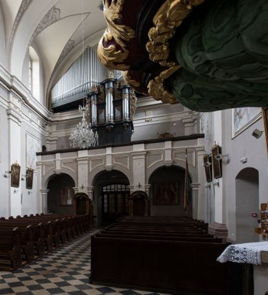 Zdjęcie nr 24: Kościół jest położony w centrum wsi, na wschód od głównej drogi, na placu otoczonym kamiennym murem przykrytym dachówką, z kilkoma drzewami. Wejście na plac przykościelny prowadzi przez szerokie schody i bramę od zachodu i bramkę od północy. Kościół jest budowlą założoną na planie prostokąta, jednonawowy, trójprzęsłowy z węższym, dwuprzęsłowym prezbiterium z apsydą. Do nawy przylegają od zachodu i północy dwie kruchty na planie kwadratu i wieża w narożu południowo-zachodnim fasady. Do prezbiterium od północy jest dostawiona kaplica na rzucie prostokąta otwierająca się półkolistymi arkadami, a od południa zakrystia. 
Artykulacja ścian jest przeprowadzona za pomocą zdwojonych pilastrów toskańskich stojących na wysokich postumentach i podtrzymujących wydatne, przełamujące się, pełne belkowanie z fryzem tryglifowym oraz wysuniętym gzymsem, obiegającym całe wnętrze świątyni. Wnętrze nakrywa sklepienie kolebkowe na gurtach z lunetami; w kluczach sklepienia znajdują się tarcze herbowe, Złota Pilawa oraz Ostoja. W lunetach umieszczone są okna prostokątne zamknięte łukiem odcinkowym; takie same okna znajdują się w apsydzie prezbiterium, poniżej belkowania.  W kaplicy znajdują się dwa prostokątne okna zamknięte odcinkowo. Zakrystia jest jednoprzestrzenna, nakryta sklepieniem krzyżowym. Prowadzi do niej kamienny portal profilowany z uszakami, z podwieszonymi wolutami, zwieńczony wydatnym gzymsem. W partii fryzu umieszczono polichromowany kartusz z herbem Ostoja. W ścianach środkowego przęsła korpusu nawowego po obu stronach kościoła znajdują się głębokie, prostokątne nisze zamknięte łukami odcinkowymi. W niszy północnej umieszczono drzwi prowadzące do niewielkiej kruchty przykrytej stropem, z dwoma małymi, okrągłymi oknami po bokach. Również po zachodniej stronie korpusu znajduje się wejście do kruchty. Ponadto na ścianach nawy oraz prezbiterium widnieją płyciny ujęte ramą profilowaną w tynku. W pierwszym od strony fasady przęśle znajduje się murowany chór muzyczny, trójarkadowy, wsparty na dwóch filarach opiętych pilastrami oraz dwóch półfilarach przylegających do ścian, sklepiony krzyżowo. 
Fasada kościoła jest płaska, zakończona gzymsem, z czterokondygnacyjną wieżą, nakrytą cebulastym hełmem z krzyżem. Boczne elewacje ujęte uskokowymi przyporami, zakończone gzymsem. Dachy dwuspadowe nad nawą i kruchtami, trójspadowe nad prezbiterium, półsferyczne nad apsydą, pulpitowe nad kaplicą i zakrystią, kryte blachą. Nad granicy nawy i prezbiterium wieloboczna wieżyczka na sygnaturkę z prześwitami, zakończona kopułą, sterczyną i kulą z krzyżem. 
