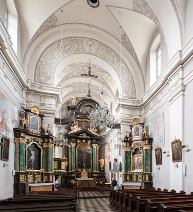 Zdjęcie nr 20: Kościół jest położony w centrum wsi, na wschód od głównej drogi, na placu otoczonym kamiennym murem przykrytym dachówką, z kilkoma drzewami. Wejście na plac przykościelny prowadzi przez szerokie schody i bramę od zachodu i bramkę od północy. Kościół jest budowlą założoną na planie prostokąta, jednonawowy, trójprzęsłowy z węższym, dwuprzęsłowym prezbiterium z apsydą. Do nawy przylegają od zachodu i północy dwie kruchty na planie kwadratu i wieża w narożu południowo-zachodnim fasady. Do prezbiterium od północy jest dostawiona kaplica na rzucie prostokąta otwierająca się półkolistymi arkadami, a od południa zakrystia. 
Artykulacja ścian jest przeprowadzona za pomocą zdwojonych pilastrów toskańskich stojących na wysokich postumentach i podtrzymujących wydatne, przełamujące się, pełne belkowanie z fryzem tryglifowym oraz wysuniętym gzymsem, obiegającym całe wnętrze świątyni. Wnętrze nakrywa sklepienie kolebkowe na gurtach z lunetami; w kluczach sklepienia znajdują się tarcze herbowe, Złota Pilawa oraz Ostoja. W lunetach umieszczone są okna prostokątne zamknięte łukiem odcinkowym; takie same okna znajdują się w apsydzie prezbiterium, poniżej belkowania.  W kaplicy znajdują się dwa prostokątne okna zamknięte odcinkowo. Zakrystia jest jednoprzestrzenna, nakryta sklepieniem krzyżowym. Prowadzi do niej kamienny portal profilowany z uszakami, z podwieszonymi wolutami, zwieńczony wydatnym gzymsem. W partii fryzu umieszczono polichromowany kartusz z herbem Ostoja. W ścianach środkowego przęsła korpusu nawowego po obu stronach kościoła znajdują się głębokie, prostokątne nisze zamknięte łukami odcinkowymi. W niszy północnej umieszczono drzwi prowadzące do niewielkiej kruchty przykrytej stropem, z dwoma małymi, okrągłymi oknami po bokach. Również po zachodniej stronie korpusu znajduje się wejście do kruchty. Ponadto na ścianach nawy oraz prezbiterium widnieją płyciny ujęte ramą profilowaną w tynku. W pierwszym od strony fasady przęśle znajduje się murowany chór muzyczny, trójarkadowy, wsparty na dwóch filarach opiętych pilastrami oraz dwóch półfilarach przylegających do ścian, sklepiony krzyżowo. 
Fasada kościoła jest płaska, zakończona gzymsem, z czterokondygnacyjną wieżą, nakrytą cebulastym hełmem z krzyżem. Boczne elewacje ujęte uskokowymi przyporami, zakończone gzymsem. Dachy dwuspadowe nad nawą i kruchtami, trójspadowe nad prezbiterium, półsferyczne nad apsydą, pulpitowe nad kaplicą i zakrystią, kryte blachą. Nad granicy nawy i prezbiterium wieloboczna wieżyczka na sygnaturkę z prześwitami, zakończona kopułą, sterczyną i kulą z krzyżem. 
