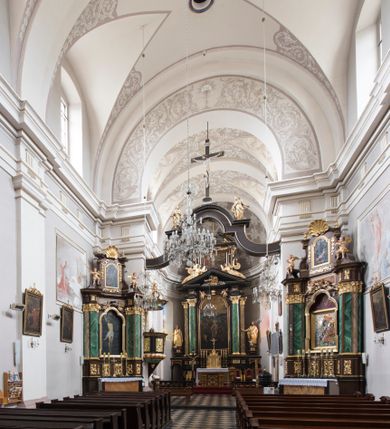 Zdjęcie nr 19: Kościół jest położony w centrum wsi, na wschód od głównej drogi, na placu otoczonym kamiennym murem przykrytym dachówką, z kilkoma drzewami. Wejście na plac przykościelny prowadzi przez szerokie schody i bramę od zachodu i bramkę od północy. Kościół jest budowlą założoną na planie prostokąta, jednonawowy, trójprzęsłowy z węższym, dwuprzęsłowym prezbiterium z apsydą. Do nawy przylegają od zachodu i północy dwie kruchty na planie kwadratu i wieża w narożu południowo-zachodnim fasady. Do prezbiterium od północy jest dostawiona kaplica na rzucie prostokąta otwierająca się półkolistymi arkadami, a od południa zakrystia. 
Artykulacja ścian jest przeprowadzona za pomocą zdwojonych pilastrów toskańskich stojących na wysokich postumentach i podtrzymujących wydatne, przełamujące się, pełne belkowanie z fryzem tryglifowym oraz wysuniętym gzymsem, obiegającym całe wnętrze świątyni. Wnętrze nakrywa sklepienie kolebkowe na gurtach z lunetami; w kluczach sklepienia znajdują się tarcze herbowe, Złota Pilawa oraz Ostoja. W lunetach umieszczone są okna prostokątne zamknięte łukiem odcinkowym; takie same okna znajdują się w apsydzie prezbiterium, poniżej belkowania.  W kaplicy znajdują się dwa prostokątne okna zamknięte odcinkowo. Zakrystia jest jednoprzestrzenna, nakryta sklepieniem krzyżowym. Prowadzi do niej kamienny portal profilowany z uszakami, z podwieszonymi wolutami, zwieńczony wydatnym gzymsem. W partii fryzu umieszczono polichromowany kartusz z herbem Ostoja. W ścianach środkowego przęsła korpusu nawowego po obu stronach kościoła znajdują się głębokie, prostokątne nisze zamknięte łukami odcinkowymi. W niszy północnej umieszczono drzwi prowadzące do niewielkiej kruchty przykrytej stropem, z dwoma małymi, okrągłymi oknami po bokach. Również po zachodniej stronie korpusu znajduje się wejście do kruchty. Ponadto na ścianach nawy oraz prezbiterium widnieją płyciny ujęte ramą profilowaną w tynku. W pierwszym od strony fasady przęśle znajduje się murowany chór muzyczny, trójarkadowy, wsparty na dwóch filarach opiętych pilastrami oraz dwóch półfilarach przylegających do ścian, sklepiony krzyżowo. 
Fasada kościoła jest płaska, zakończona gzymsem, z czterokondygnacyjną wieżą, nakrytą cebulastym hełmem z krzyżem. Boczne elewacje ujęte uskokowymi przyporami, zakończone gzymsem. Dachy dwuspadowe nad nawą i kruchtami, trójspadowe nad prezbiterium, półsferyczne nad apsydą, pulpitowe nad kaplicą i zakrystią, kryte blachą. Nad granicy nawy i prezbiterium wieloboczna wieżyczka na sygnaturkę z prześwitami, zakończona kopułą, sterczyną i kulą z krzyżem. 
