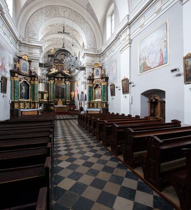 Zdjęcie nr 26: Kościół jest położony w centrum wsi, na wschód od głównej drogi, na placu otoczonym kamiennym murem przykrytym dachówką, z kilkoma drzewami. Wejście na plac przykościelny prowadzi przez szerokie schody i bramę od zachodu i bramkę od północy. Kościół jest budowlą założoną na planie prostokąta, jednonawowy, trójprzęsłowy z węższym, dwuprzęsłowym prezbiterium z apsydą. Do nawy przylegają od zachodu i północy dwie kruchty na planie kwadratu i wieża w narożu południowo-zachodnim fasady. Do prezbiterium od północy jest dostawiona kaplica na rzucie prostokąta otwierająca się półkolistymi arkadami, a od południa zakrystia. 
Artykulacja ścian jest przeprowadzona za pomocą zdwojonych pilastrów toskańskich stojących na wysokich postumentach i podtrzymujących wydatne, przełamujące się, pełne belkowanie z fryzem tryglifowym oraz wysuniętym gzymsem, obiegającym całe wnętrze świątyni. Wnętrze nakrywa sklepienie kolebkowe na gurtach z lunetami; w kluczach sklepienia znajdują się tarcze herbowe, Złota Pilawa oraz Ostoja. W lunetach umieszczone są okna prostokątne zamknięte łukiem odcinkowym; takie same okna znajdują się w apsydzie prezbiterium, poniżej belkowania.  W kaplicy znajdują się dwa prostokątne okna zamknięte odcinkowo. Zakrystia jest jednoprzestrzenna, nakryta sklepieniem krzyżowym. Prowadzi do niej kamienny portal profilowany z uszakami, z podwieszonymi wolutami, zwieńczony wydatnym gzymsem. W partii fryzu umieszczono polichromowany kartusz z herbem Ostoja. W ścianach środkowego przęsła korpusu nawowego po obu stronach kościoła znajdują się głębokie, prostokątne nisze zamknięte łukami odcinkowymi. W niszy północnej umieszczono drzwi prowadzące do niewielkiej kruchty przykrytej stropem, z dwoma małymi, okrągłymi oknami po bokach. Również po zachodniej stronie korpusu znajduje się wejście do kruchty. Ponadto na ścianach nawy oraz prezbiterium widnieją płyciny ujęte ramą profilowaną w tynku. W pierwszym od strony fasady przęśle znajduje się murowany chór muzyczny, trójarkadowy, wsparty na dwóch filarach opiętych pilastrami oraz dwóch półfilarach przylegających do ścian, sklepiony krzyżowo. 
Fasada kościoła jest płaska, zakończona gzymsem, z czterokondygnacyjną wieżą, nakrytą cebulastym hełmem z krzyżem. Boczne elewacje ujęte uskokowymi przyporami, zakończone gzymsem. Dachy dwuspadowe nad nawą i kruchtami, trójspadowe nad prezbiterium, półsferyczne nad apsydą, pulpitowe nad kaplicą i zakrystią, kryte blachą. Nad granicy nawy i prezbiterium wieloboczna wieżyczka na sygnaturkę z prześwitami, zakończona kopułą, sterczyną i kulą z krzyżem. 
