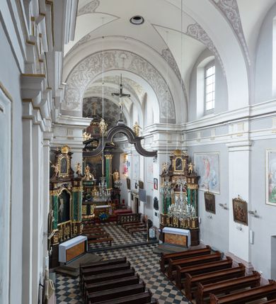 Zdjęcie nr 3: Kościół jest położony w centrum wsi, na wschód od głównej drogi, na placu otoczonym kamiennym murem przykrytym dachówką, z kilkoma drzewami. Wejście na plac przykościelny prowadzi przez szerokie schody i bramę od zachodu i bramkę od północy. Kościół jest budowlą założoną na planie prostokąta, jednonawowy, trójprzęsłowy z węższym, dwuprzęsłowym prezbiterium z apsydą. Do nawy przylegają od zachodu i północy dwie kruchty na planie kwadratu i wieża w narożu południowo-zachodnim fasady. Do prezbiterium od północy jest dostawiona kaplica na rzucie prostokąta otwierająca się półkolistymi arkadami, a od południa zakrystia. 
Artykulacja ścian jest przeprowadzona za pomocą zdwojonych pilastrów toskańskich stojących na wysokich postumentach i podtrzymujących wydatne, przełamujące się, pełne belkowanie z fryzem tryglifowym oraz wysuniętym gzymsem, obiegającym całe wnętrze świątyni. Wnętrze nakrywa sklepienie kolebkowe na gurtach z lunetami; w kluczach sklepienia znajdują się tarcze herbowe, Złota Pilawa oraz Ostoja. W lunetach umieszczone są okna prostokątne zamknięte łukiem odcinkowym; takie same okna znajdują się w apsydzie prezbiterium, poniżej belkowania.  W kaplicy znajdują się dwa prostokątne okna zamknięte odcinkowo. Zakrystia jest jednoprzestrzenna, nakryta sklepieniem krzyżowym. Prowadzi do niej kamienny portal profilowany z uszakami, z podwieszonymi wolutami, zwieńczony wydatnym gzymsem. W partii fryzu umieszczono polichromowany kartusz z herbem Ostoja. W ścianach środkowego przęsła korpusu nawowego po obu stronach kościoła znajdują się głębokie, prostokątne nisze zamknięte łukami odcinkowymi. W niszy północnej umieszczono drzwi prowadzące do niewielkiej kruchty przykrytej stropem, z dwoma małymi, okrągłymi oknami po bokach. Również po zachodniej stronie korpusu znajduje się wejście do kruchty. Ponadto na ścianach nawy oraz prezbiterium widnieją płyciny ujęte ramą profilowaną w tynku. W pierwszym od strony fasady przęśle znajduje się murowany chór muzyczny, trójarkadowy, wsparty na dwóch filarach opiętych pilastrami oraz dwóch półfilarach przylegających do ścian, sklepiony krzyżowo. 
Fasada kościoła jest płaska, zakończona gzymsem, z czterokondygnacyjną wieżą, nakrytą cebulastym hełmem z krzyżem. Boczne elewacje ujęte uskokowymi przyporami, zakończone gzymsem. Dachy dwuspadowe nad nawą i kruchtami, trójspadowe nad prezbiterium, półsferyczne nad apsydą, pulpitowe nad kaplicą i zakrystią, kryte blachą. Nad granicy nawy i prezbiterium wieloboczna wieżyczka na sygnaturkę z prześwitami, zakończona kopułą, sterczyną i kulą z krzyżem. 
