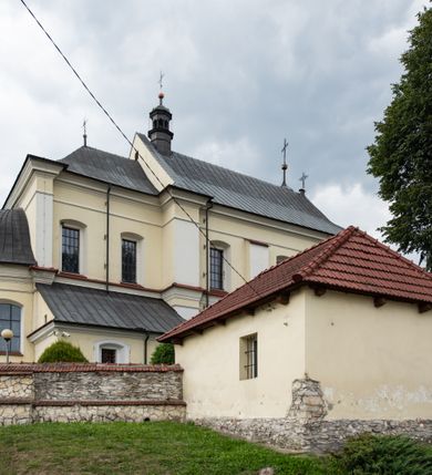 Zdjęcie nr 28: Kościół jest położony w centrum wsi, na wschód od głównej drogi, na placu otoczonym kamiennym murem przykrytym dachówką, z kilkoma drzewami. Wejście na plac przykościelny prowadzi przez szerokie schody i bramę od zachodu i bramkę od północy. Kościół jest budowlą założoną na planie prostokąta, jednonawowy, trójprzęsłowy z węższym, dwuprzęsłowym prezbiterium z apsydą. Do nawy przylegają od zachodu i północy dwie kruchty na planie kwadratu i wieża w narożu południowo-zachodnim fasady. Do prezbiterium od północy jest dostawiona kaplica na rzucie prostokąta otwierająca się półkolistymi arkadami, a od południa zakrystia. 
Artykulacja ścian jest przeprowadzona za pomocą zdwojonych pilastrów toskańskich stojących na wysokich postumentach i podtrzymujących wydatne, przełamujące się, pełne belkowanie z fryzem tryglifowym oraz wysuniętym gzymsem, obiegającym całe wnętrze świątyni. Wnętrze nakrywa sklepienie kolebkowe na gurtach z lunetami; w kluczach sklepienia znajdują się tarcze herbowe, Złota Pilawa oraz Ostoja. W lunetach umieszczone są okna prostokątne zamknięte łukiem odcinkowym; takie same okna znajdują się w apsydzie prezbiterium, poniżej belkowania.  W kaplicy znajdują się dwa prostokątne okna zamknięte odcinkowo. Zakrystia jest jednoprzestrzenna, nakryta sklepieniem krzyżowym. Prowadzi do niej kamienny portal profilowany z uszakami, z podwieszonymi wolutami, zwieńczony wydatnym gzymsem. W partii fryzu umieszczono polichromowany kartusz z herbem Ostoja. W ścianach środkowego przęsła korpusu nawowego po obu stronach kościoła znajdują się głębokie, prostokątne nisze zamknięte łukami odcinkowymi. W niszy północnej umieszczono drzwi prowadzące do niewielkiej kruchty przykrytej stropem, z dwoma małymi, okrągłymi oknami po bokach. Również po zachodniej stronie korpusu znajduje się wejście do kruchty. Ponadto na ścianach nawy oraz prezbiterium widnieją płyciny ujęte ramą profilowaną w tynku. W pierwszym od strony fasady przęśle znajduje się murowany chór muzyczny, trójarkadowy, wsparty na dwóch filarach opiętych pilastrami oraz dwóch półfilarach przylegających do ścian, sklepiony krzyżowo. 
Fasada kościoła jest płaska, zakończona gzymsem, z czterokondygnacyjną wieżą, nakrytą cebulastym hełmem z krzyżem. Boczne elewacje ujęte uskokowymi przyporami, zakończone gzymsem. Dachy dwuspadowe nad nawą i kruchtami, trójspadowe nad prezbiterium, półsferyczne nad apsydą, pulpitowe nad kaplicą i zakrystią, kryte blachą. Nad granicy nawy i prezbiterium wieloboczna wieżyczka na sygnaturkę z prześwitami, zakończona kopułą, sterczyną i kulą z krzyżem. 
