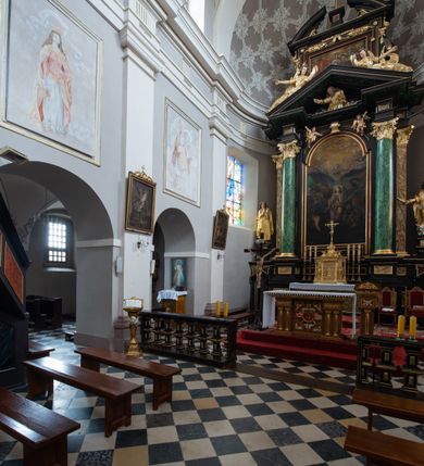 Zdjęcie nr 9: Kościół jest położony w centrum wsi, na wschód od głównej drogi, na placu otoczonym kamiennym murem przykrytym dachówką, z kilkoma drzewami. Wejście na plac przykościelny prowadzi przez szerokie schody i bramę od zachodu i bramkę od północy. Kościół jest budowlą założoną na planie prostokąta, jednonawowy, trójprzęsłowy z węższym, dwuprzęsłowym prezbiterium z apsydą. Do nawy przylegają od zachodu i północy dwie kruchty na planie kwadratu i wieża w narożu południowo-zachodnim fasady. Do prezbiterium od północy jest dostawiona kaplica na rzucie prostokąta otwierająca się półkolistymi arkadami, a od południa zakrystia. 
Artykulacja ścian jest przeprowadzona za pomocą zdwojonych pilastrów toskańskich stojących na wysokich postumentach i podtrzymujących wydatne, przełamujące się, pełne belkowanie z fryzem tryglifowym oraz wysuniętym gzymsem, obiegającym całe wnętrze świątyni. Wnętrze nakrywa sklepienie kolebkowe na gurtach z lunetami; w kluczach sklepienia znajdują się tarcze herbowe, Złota Pilawa oraz Ostoja. W lunetach umieszczone są okna prostokątne zamknięte łukiem odcinkowym; takie same okna znajdują się w apsydzie prezbiterium, poniżej belkowania.  W kaplicy znajdują się dwa prostokątne okna zamknięte odcinkowo. Zakrystia jest jednoprzestrzenna, nakryta sklepieniem krzyżowym. Prowadzi do niej kamienny portal profilowany z uszakami, z podwieszonymi wolutami, zwieńczony wydatnym gzymsem. W partii fryzu umieszczono polichromowany kartusz z herbem Ostoja. W ścianach środkowego przęsła korpusu nawowego po obu stronach kościoła znajdują się głębokie, prostokątne nisze zamknięte łukami odcinkowymi. W niszy północnej umieszczono drzwi prowadzące do niewielkiej kruchty przykrytej stropem, z dwoma małymi, okrągłymi oknami po bokach. Również po zachodniej stronie korpusu znajduje się wejście do kruchty. Ponadto na ścianach nawy oraz prezbiterium widnieją płyciny ujęte ramą profilowaną w tynku. W pierwszym od strony fasady przęśle znajduje się murowany chór muzyczny, trójarkadowy, wsparty na dwóch filarach opiętych pilastrami oraz dwóch półfilarach przylegających do ścian, sklepiony krzyżowo. 
Fasada kościoła jest płaska, zakończona gzymsem, z czterokondygnacyjną wieżą, nakrytą cebulastym hełmem z krzyżem. Boczne elewacje ujęte uskokowymi przyporami, zakończone gzymsem. Dachy dwuspadowe nad nawą i kruchtami, trójspadowe nad prezbiterium, półsferyczne nad apsydą, pulpitowe nad kaplicą i zakrystią, kryte blachą. Nad granicy nawy i prezbiterium wieloboczna wieżyczka na sygnaturkę z prześwitami, zakończona kopułą, sterczyną i kulą z krzyżem. 
