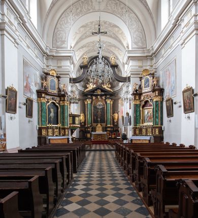 Zdjęcie nr 13: Kościół jest położony w centrum wsi, na wschód od głównej drogi, na placu otoczonym kamiennym murem przykrytym dachówką, z kilkoma drzewami. Wejście na plac przykościelny prowadzi przez szerokie schody i bramę od zachodu i bramkę od północy. Kościół jest budowlą założoną na planie prostokąta, jednonawowy, trójprzęsłowy z węższym, dwuprzęsłowym prezbiterium z apsydą. Do nawy przylegają od zachodu i północy dwie kruchty na planie kwadratu i wieża w narożu południowo-zachodnim fasady. Do prezbiterium od północy jest dostawiona kaplica na rzucie prostokąta otwierająca się półkolistymi arkadami, a od południa zakrystia. 
Artykulacja ścian jest przeprowadzona za pomocą zdwojonych pilastrów toskańskich stojących na wysokich postumentach i podtrzymujących wydatne, przełamujące się, pełne belkowanie z fryzem tryglifowym oraz wysuniętym gzymsem, obiegającym całe wnętrze świątyni. Wnętrze nakrywa sklepienie kolebkowe na gurtach z lunetami; w kluczach sklepienia znajdują się tarcze herbowe, Złota Pilawa oraz Ostoja. W lunetach umieszczone są okna prostokątne zamknięte łukiem odcinkowym; takie same okna znajdują się w apsydzie prezbiterium, poniżej belkowania.  W kaplicy znajdują się dwa prostokątne okna zamknięte odcinkowo. Zakrystia jest jednoprzestrzenna, nakryta sklepieniem krzyżowym. Prowadzi do niej kamienny portal profilowany z uszakami, z podwieszonymi wolutami, zwieńczony wydatnym gzymsem. W partii fryzu umieszczono polichromowany kartusz z herbem Ostoja. W ścianach środkowego przęsła korpusu nawowego po obu stronach kościoła znajdują się głębokie, prostokątne nisze zamknięte łukami odcinkowymi. W niszy północnej umieszczono drzwi prowadzące do niewielkiej kruchty przykrytej stropem, z dwoma małymi, okrągłymi oknami po bokach. Również po zachodniej stronie korpusu znajduje się wejście do kruchty. Ponadto na ścianach nawy oraz prezbiterium widnieją płyciny ujęte ramą profilowaną w tynku. W pierwszym od strony fasady przęśle znajduje się murowany chór muzyczny, trójarkadowy, wsparty na dwóch filarach opiętych pilastrami oraz dwóch półfilarach przylegających do ścian, sklepiony krzyżowo. 
Fasada kościoła jest płaska, zakończona gzymsem, z czterokondygnacyjną wieżą, nakrytą cebulastym hełmem z krzyżem. Boczne elewacje ujęte uskokowymi przyporami, zakończone gzymsem. Dachy dwuspadowe nad nawą i kruchtami, trójspadowe nad prezbiterium, półsferyczne nad apsydą, pulpitowe nad kaplicą i zakrystią, kryte blachą. Nad granicy nawy i prezbiterium wieloboczna wieżyczka na sygnaturkę z prześwitami, zakończona kopułą, sterczyną i kulą z krzyżem. 
