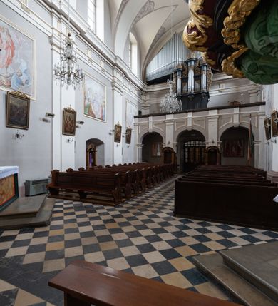 Zdjęcie nr 11: Kościół jest położony w centrum wsi, na wschód od głównej drogi, na placu otoczonym kamiennym murem przykrytym dachówką, z kilkoma drzewami. Wejście na plac przykościelny prowadzi przez szerokie schody i bramę od zachodu i bramkę od północy. Kościół jest budowlą założoną na planie prostokąta, jednonawowy, trójprzęsłowy z węższym, dwuprzęsłowym prezbiterium z apsydą. Do nawy przylegają od zachodu i północy dwie kruchty na planie kwadratu i wieża w narożu południowo-zachodnim fasady. Do prezbiterium od północy jest dostawiona kaplica na rzucie prostokąta otwierająca się półkolistymi arkadami, a od południa zakrystia. 
Artykulacja ścian jest przeprowadzona za pomocą zdwojonych pilastrów toskańskich stojących na wysokich postumentach i podtrzymujących wydatne, przełamujące się, pełne belkowanie z fryzem tryglifowym oraz wysuniętym gzymsem, obiegającym całe wnętrze świątyni. Wnętrze nakrywa sklepienie kolebkowe na gurtach z lunetami; w kluczach sklepienia znajdują się tarcze herbowe, Złota Pilawa oraz Ostoja. W lunetach umieszczone są okna prostokątne zamknięte łukiem odcinkowym; takie same okna znajdują się w apsydzie prezbiterium, poniżej belkowania.  W kaplicy znajdują się dwa prostokątne okna zamknięte odcinkowo. Zakrystia jest jednoprzestrzenna, nakryta sklepieniem krzyżowym. Prowadzi do niej kamienny portal profilowany z uszakami, z podwieszonymi wolutami, zwieńczony wydatnym gzymsem. W partii fryzu umieszczono polichromowany kartusz z herbem Ostoja. W ścianach środkowego przęsła korpusu nawowego po obu stronach kościoła znajdują się głębokie, prostokątne nisze zamknięte łukami odcinkowymi. W niszy północnej umieszczono drzwi prowadzące do niewielkiej kruchty przykrytej stropem, z dwoma małymi, okrągłymi oknami po bokach. Również po zachodniej stronie korpusu znajduje się wejście do kruchty. Ponadto na ścianach nawy oraz prezbiterium widnieją płyciny ujęte ramą profilowaną w tynku. W pierwszym od strony fasady przęśle znajduje się murowany chór muzyczny, trójarkadowy, wsparty na dwóch filarach opiętych pilastrami oraz dwóch półfilarach przylegających do ścian, sklepiony krzyżowo. 
Fasada kościoła jest płaska, zakończona gzymsem, z czterokondygnacyjną wieżą, nakrytą cebulastym hełmem z krzyżem. Boczne elewacje ujęte uskokowymi przyporami, zakończone gzymsem. Dachy dwuspadowe nad nawą i kruchtami, trójspadowe nad prezbiterium, półsferyczne nad apsydą, pulpitowe nad kaplicą i zakrystią, kryte blachą. Nad granicy nawy i prezbiterium wieloboczna wieżyczka na sygnaturkę z prześwitami, zakończona kopułą, sterczyną i kulą z krzyżem. 
