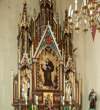 Zdjęcie nr 3: Ołtarz drewniany, prostopadłościenny, na dwustopniowej podstawie; mensa drewniana; antependium podzielone na trzy kwadratowe pola wypełnione maswerkami. 

Tabernakulum w formie prostopadłościennej skrzynki. Ścianka frontowa flankowana dwiema lizenami dźwigającymi niepełne belkowanie wyłamane nad osią środkową, opasujące tabernakulum z trzech stron, z fryzem dekorowanym maswerkowymi czwórliśćmi. Drzwiczki w formie stojącego prostokąta, zamkniętego łukiem ostrym z płaskorzeźbionym krzyżem w polu. 

Nastawa architektoniczna, jednoosiowa, jednokondygnacyjna ze zwieńczeniem, z predellą. Kondygnacja ujęta parą dwustrefowych kapliczek: w dolnej części, w niszach zwieńczonych wimpergą figury św. Wojciecha i św. Stanisława; w górnej zamknięte od góry baldachimem z ażurową fialą, zdobioną maswerkiem, sterczynami i wimpergami. Pole środkowe nastawy na cokole, ujęte wysokimi, wąskimi kolumienkami podtrzymującymi ostrołukową arkadę z niszą, zwieńczoną wimpergą. Wimperga wypełniona maswerkiem z czwórliściem pośrodku. W niszy obraz św. Antoniego Padewskiego, na zasuwie obraz Jezusa Miłosiernego. Kondygnację ujmują uszy w postaci łuków przyporowych, zdobionych ażurowymi blendami i sterczynami. Zwieńczenie w formie wieżyczki flankowane łukami przyporowymi, zakończone wysoką fialą z kwiatonem.

Struktura w kolorze naturalnego drewna, płyciny polichromowane na czerwono i niebiesko; kolumienki, ornamentyka, profile i detale architektoniczne złocone.
