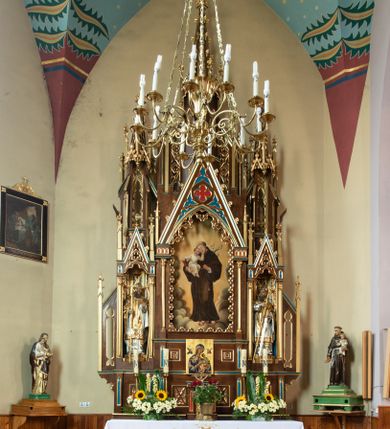 Zdjęcie nr 1: Ołtarz drewniany, prostopadłościenny, na dwustopniowej podstawie; mensa drewniana; antependium podzielone na trzy kwadratowe pola wypełnione maswerkami. 

Tabernakulum w formie prostopadłościennej skrzynki. Ścianka frontowa flankowana dwiema lizenami dźwigającymi niepełne belkowanie wyłamane nad osią środkową, opasujące tabernakulum z trzech stron, z fryzem dekorowanym maswerkowymi czwórliśćmi. Drzwiczki w formie stojącego prostokąta, zamkniętego łukiem ostrym z płaskorzeźbionym krzyżem w polu. 

Nastawa architektoniczna, jednoosiowa, jednokondygnacyjna ze zwieńczeniem, z predellą. Kondygnacja ujęta parą dwustrefowych kapliczek: w dolnej części, w niszach zwieńczonych wimpergą figury św. Wojciecha i św. Stanisława; w górnej zamknięte od góry baldachimem z ażurową fialą, zdobioną maswerkiem, sterczynami i wimpergami. Pole środkowe nastawy na cokole, ujęte wysokimi, wąskimi kolumienkami podtrzymującymi ostrołukową arkadę z niszą, zwieńczoną wimpergą. Wimperga wypełniona maswerkiem z czwórliściem pośrodku. W niszy obraz św. Antoniego Padewskiego, na zasuwie obraz Jezusa Miłosiernego. Kondygnację ujmują uszy w postaci łuków przyporowych, zdobionych ażurowymi blendami i sterczynami. Zwieńczenie w formie wieżyczki flankowane łukami przyporowymi, zakończone wysoką fialą z kwiatonem.

Struktura w kolorze naturalnego drewna, płyciny polichromowane na czerwono i niebiesko; kolumienki, ornamentyka, profile i detale architektoniczne złocone.
