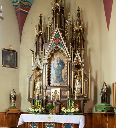 Zdjęcie nr 2: Ołtarz drewniany, prostopadłościenny, na dwustopniowej podstawie; mensa drewniana; antependium podzielone na trzy kwadratowe pola wypełnione maswerkami. 

Tabernakulum w formie prostopadłościennej skrzynki. Ścianka frontowa flankowana dwiema lizenami dźwigającymi niepełne belkowanie wyłamane nad osią środkową, opasujące tabernakulum z trzech stron, z fryzem dekorowanym maswerkowymi czwórliśćmi. Drzwiczki w formie stojącego prostokąta, zamkniętego łukiem ostrym z płaskorzeźbionym krzyżem w polu. 

Nastawa architektoniczna, jednoosiowa, jednokondygnacyjna ze zwieńczeniem, z predellą. Kondygnacja ujęta parą dwustrefowych kapliczek: w dolnej części, w niszach zwieńczonych wimpergą figury św. Wojciecha i św. Stanisława; w górnej zamknięte od góry baldachimem z ażurową fialą, zdobioną maswerkiem, sterczynami i wimpergami. Pole środkowe nastawy na cokole, ujęte wysokimi, wąskimi kolumienkami podtrzymującymi ostrołukową arkadę z niszą, zwieńczoną wimpergą. Wimperga wypełniona maswerkiem z czwórliściem pośrodku. W niszy obraz św. Antoniego Padewskiego, na zasuwie obraz Jezusa Miłosiernego. Kondygnację ujmują uszy w postaci łuków przyporowych, zdobionych ażurowymi blendami i sterczynami. Zwieńczenie w formie wieżyczki flankowane łukami przyporowymi, zakończone wysoką fialą z kwiatonem.

Struktura w kolorze naturalnego drewna, płyciny polichromowane na czerwono i niebiesko; kolumienki, ornamentyka, profile i detale architektoniczne złocone.
