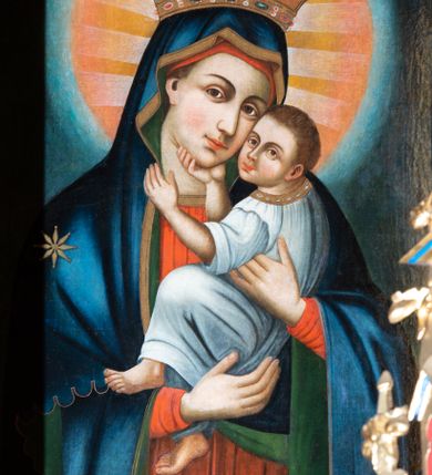 Zdjęcie nr 1: Obraz w kształcie prostokąta stojącego z przedstawieniem Matki Boskiej z Dzieciątkiem w typie Eleusy. W centrum ukazana Matka Boska w półpostaci, zwrócona delikatnie w lewo, z pochyloną głową w stronę Dzieciątka, które trzyma na rękach. Twarz owalna o mocno zaznaczonych rysach nosa i łuków brwiowych, wzrok skierowany na wprost. Ubrana w czerwoną suknię ze złotą lamówką, obficie drapowaną oraz granatowy maforion ze złotą lamówką zarzucony na głowę i ramiona z gwiazdą na prawym ramieniu. Dzieciątko Jezus ukazane z lewego profilu, przytula twarz do twarzy Matki Boskiej, prawą ręką ujmuje jej brodę, a lewą szyję. Ma twarz owalną o wyrazistych rysach. Ubrane jest w białą szatę z rękawami podwiniętymi do łokci. Wokół głowy Matki Boskiej duży złoto-czerwony nimb. Tło jednolite, granatowe. Kolorystyka intensywna, silny linearyzm.
