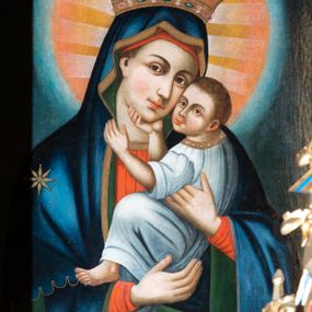 Zdjęcie nr 1: Obraz w kształcie prostokąta stojącego z przedstawieniem Matki Boskiej z Dzieciątkiem w typie Eleusy. W centrum ukazana Matka Boska w półpostaci, zwrócona delikatnie w lewo, z pochyloną głową w stronę Dzieciątka, które trzyma na rękach. Twarz owalna o mocno zaznaczonych rysach nosa i łuków brwiowych, wzrok skierowany na wprost. Ubrana w czerwoną suknię ze złotą lamówką, obficie drapowaną oraz granatowy maforion ze złotą lamówką zarzucony na głowę i ramiona z gwiazdą na prawym ramieniu. Dzieciątko Jezus ukazane z lewego profilu, przytula twarz do twarzy Matki Boskiej, prawą ręką ujmuje jej brodę, a lewą szyję. Ma twarz owalną o wyrazistych rysach. Ubrane jest w białą szatę z rękawami podwiniętymi do łokci. Wokół głowy Matki Boskiej duży złoto-czerwony nimb. Tło jednolite, granatowe. Kolorystyka intensywna, silny linearyzm.
