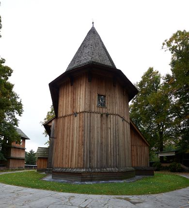 Zdjęcie nr 9: Kościół drewniany, orientowany, usytuowany na wzgórku, otoczony pierwotnym cmentarzem przykościelnym oraz starodrzewiem (lipami), ujęty drewnianym ogrodzeniem z poziomo ułożonych desek, w którego ciągu znajduje się masywna dzwonnica. Ściany kościoła wzniesione w konstrukcji zrębowej, oszalowanej pionowo z listwowaniem. Nawa na planie prostokąta; prezbiterium węższe, zamknięte wielobocznie, zbudowane na zrąb; od północy zakrystia na planie prostokąta; od południa późniejsza, dobudowana kruchta. Od zachodu nawę poprzedza niższa wieża, zbudowana w konstrukcji słupowo-ramowej, o pochyłych ścianach. Wnętrze nakryte stropami, w nawie z zaskrzynieniami. Nawa od prezbiterium oddzielona tęczą o łuku półkolistym wspartym na kroksztynach; na belce umieszczone rzeźby z początku XVI wieku przedstawiające grupę Ukrzyżowania: krucyfiks, Matka Boska, św. Jan Ewangelista oraz św. Maria Magdalena. Chór muzyczny wsparty na dwóch kolumnach, barokowy. Wnętrze pokryte polichromią z pierwszej połowy XVII wieku. Pośrodku kościoła oraz bliżej chóru muzycznego znajdują się wejścia do krypt pokryte płytami. Główny portal kościoła umieszczony jest od strony zachodniej, w przedsionku pod wieżą, ukształtowany w formie profilowanej, lekko zaostrzonej arkady przechodzącej w tzw. ośli grzbiet. Portal południowy, w kruchcie zakończony ostrołukiem, z motywem sznura w profilowaniach z pierwotnymi jednoskrzydłowymi drzwiami o gotyckich okuciach. Portal prowadzący z prezbiterium do zakrystii ma bogate profilowanie (zewnętrzny profil z motywem „ząbków”), jest zakończony w tzw. ośli grzbiet z drzwiami żelaznymi, dekorowanymi ukośną kratą. Okna znajdują się od strony południowej, pod dwa w nawie oraz w prezbiterium. Nadokienniki mają wykrój w ośli grzbiet. Ponadto jedno okno o analogicznym układzie w prezbiterium na ścianie wschodniej, częściowo zabudowane, zasłonięte ołtarzem. Dach gontowy o jednej kalenicy, wsparty na kroksztynach z szerokim okapem, o dużym kącie spadku uzyskanym poprzez zastosowaną gotycką więźbę storczykową, pośrodku z wieżyczką na sygnaturkę o barkowym kształcie. Wieża główna nakryta dachem gontowym, trójspadowym.
