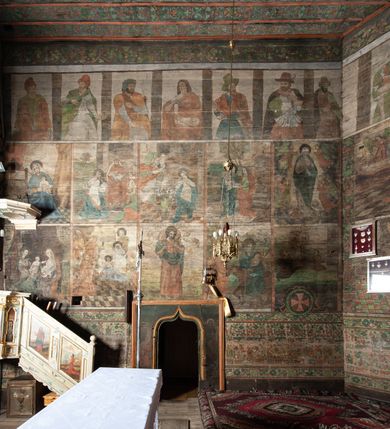 Zdjęcie nr 16: Kościół drewniany, orientowany, usytuowany na wzgórku, otoczony pierwotnym cmentarzem przykościelnym oraz starodrzewiem (lipami), ujęty drewnianym ogrodzeniem z poziomo ułożonych desek, w którego ciągu znajduje się masywna dzwonnica. Ściany kościoła wzniesione w konstrukcji zrębowej, oszalowanej pionowo z listwowaniem. Nawa na planie prostokąta; prezbiterium węższe, zamknięte wielobocznie, zbudowane na zrąb; od północy zakrystia na planie prostokąta; od południa późniejsza, dobudowana kruchta. Od zachodu nawę poprzedza niższa wieża, zbudowana w konstrukcji słupowo-ramowej, o pochyłych ścianach. Wnętrze nakryte stropami, w nawie z zaskrzynieniami. Nawa od prezbiterium oddzielona tęczą o łuku półkolistym wspartym na kroksztynach; na belce umieszczone rzeźby z początku XVI wieku przedstawiające grupę Ukrzyżowania: krucyfiks, Matka Boska, św. Jan Ewangelista oraz św. Maria Magdalena. Chór muzyczny wsparty na dwóch kolumnach, barokowy. Wnętrze pokryte polichromią z pierwszej połowy XVII wieku. Pośrodku kościoła oraz bliżej chóru muzycznego znajdują się wejścia do krypt pokryte płytami. Główny portal kościoła umieszczony jest od strony zachodniej, w przedsionku pod wieżą, ukształtowany w formie profilowanej, lekko zaostrzonej arkady przechodzącej w tzw. ośli grzbiet. Portal południowy, w kruchcie zakończony ostrołukiem, z motywem sznura w profilowaniach z pierwotnymi jednoskrzydłowymi drzwiami o gotyckich okuciach. Portal prowadzący z prezbiterium do zakrystii ma bogate profilowanie (zewnętrzny profil z motywem „ząbków”), jest zakończony w tzw. ośli grzbiet z drzwiami żelaznymi, dekorowanymi ukośną kratą. Okna znajdują się od strony południowej, pod dwa w nawie oraz w prezbiterium. Nadokienniki mają wykrój w ośli grzbiet. Ponadto jedno okno o analogicznym układzie w prezbiterium na ścianie wschodniej, częściowo zabudowane, zasłonięte ołtarzem. Dach gontowy o jednej kalenicy, wsparty na kroksztynach z szerokim okapem, o dużym kącie spadku uzyskanym poprzez zastosowaną gotycką więźbę storczykową, pośrodku z wieżyczką na sygnaturkę o barkowym kształcie. Wieża główna nakryta dachem gontowym, trójspadowym.
