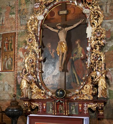 Zdjęcie nr 2: Nastawa ołtarzowa jednoosiowa, jednokondygnacyjna. Ołtarz prostopadłościenny, drewniany. Mensa z przodu dekorowana płyciną w kształcie prostokąta leżącego, malowaną na czerwono, w polu dwie gałązki palmowe i monogram IHS. Nastawa ustawiona jest na niskiej, trójosiowej predelli. Na osi głównej niewielkie tempietto, wsparte sześcioma kolumienkami z figurą Chrystusa Frasobliwego wewnątrz. Po bokach dwa obrazki z klęczącymi postaciami aniołów. Na osiach bocznych spływy wolutowe z półleżącymi postaciami aniołów oraz konsolki zdobione uskrzydlonymi główkami aniołków, skierowanymi na wprost. Predella podtrzymuje krucyfiks ustawiony na tle owalnego obrazu z Grupą Ukrzyżowania, obwiedzionego dokoła ramą z narzędziami Męki Pańskiej oraz bujną dekoracją ornamentu akantowego. Insygnia Arma Christii, kolejno od dołu, po lewej: obcęgi i młotek, pochodnia, włócznia z łańcuchem, kolumna, miecz z uchem Malchusa, rękawica, misa Piłata, Veraicon, misa z kośćmi do gry, suknia i drabina w jej tle, dzban Piłata, łańcuch i trzcina. U stóp krzyża napis: „Altare Confraternitatis Paupertatis Jesu Anno Dni 1703”. Po bokach dwie rzeźby aniołów. U dołu krzyża glob ziemski, opleciony przez węża; u góry na szczycie Veraikon i tarcza herbowa z herbem Szreniawa i literami „A. S. P. R.”. Dekoracja ornamentalna predelli okuciowa z kaboszonami, w kondygnacji akantowa. Polichromia struktury w kolorze bordowym, ornamentyka i profilowania złocone i srebrzone, detale czerwone.
