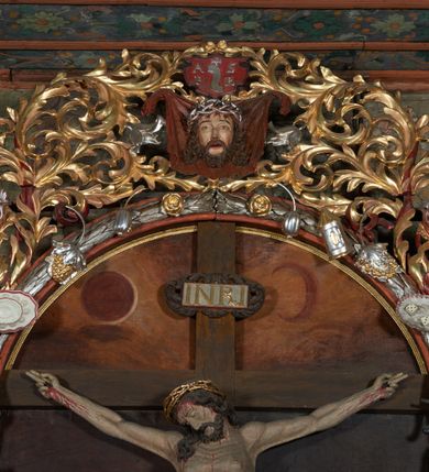 Zdjęcie nr 13: Nastawa ołtarzowa jednoosiowa, jednokondygnacyjna. Ołtarz prostopadłościenny, drewniany. Mensa z przodu dekorowana płyciną w kształcie prostokąta leżącego, malowaną na czerwono, w polu dwie gałązki palmowe i monogram IHS. Nastawa ustawiona jest na niskiej, trójosiowej predelli. Na osi głównej niewielkie tempietto, wsparte sześcioma kolumienkami z figurą Chrystusa Frasobliwego wewnątrz. Po bokach dwa obrazki z klęczącymi postaciami aniołów. Na osiach bocznych spływy wolutowe z półleżącymi postaciami aniołów oraz konsolki zdobione uskrzydlonymi główkami aniołków, skierowanymi na wprost. Predella podtrzymuje krucyfiks ustawiony na tle owalnego obrazu z Grupą Ukrzyżowania, obwiedzionego dokoła ramą z narzędziami Męki Pańskiej oraz bujną dekoracją ornamentu akantowego. Insygnia Arma Christii, kolejno od dołu, po lewej: obcęgi i młotek, pochodnia, włócznia z łańcuchem, kolumna, miecz z uchem Malchusa, rękawica, misa Piłata, Veraicon, misa z kośćmi do gry, suknia i drabina w jej tle, dzban Piłata, łańcuch i trzcina. U stóp krzyża napis: „Altare Confraternitatis Paupertatis Jesu Anno Dni 1703”. Po bokach dwie rzeźby aniołów. U dołu krzyża glob ziemski, opleciony przez węża; u góry na szczycie Veraikon i tarcza herbowa z herbem Szreniawa i literami „A. S. P. R.”. Dekoracja ornamentalna predelli okuciowa z kaboszonami, w kondygnacji akantowa. Polichromia struktury w kolorze bordowym, ornamentyka i profilowania złocone i srebrzone, detale czerwone.
