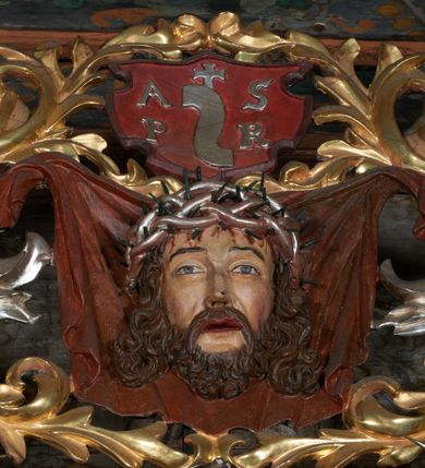 Zdjęcie nr 11: Nastawa ołtarzowa jednoosiowa, jednokondygnacyjna. Ołtarz prostopadłościenny, drewniany. Mensa z przodu dekorowana płyciną w kształcie prostokąta leżącego, malowaną na czerwono, w polu dwie gałązki palmowe i monogram IHS. Nastawa ustawiona jest na niskiej, trójosiowej predelli. Na osi głównej niewielkie tempietto, wsparte sześcioma kolumienkami z figurą Chrystusa Frasobliwego wewnątrz. Po bokach dwa obrazki z klęczącymi postaciami aniołów. Na osiach bocznych spływy wolutowe z półleżącymi postaciami aniołów oraz konsolki zdobione uskrzydlonymi główkami aniołków, skierowanymi na wprost. Predella podtrzymuje krucyfiks ustawiony na tle owalnego obrazu z Grupą Ukrzyżowania, obwiedzionego dokoła ramą z narzędziami Męki Pańskiej oraz bujną dekoracją ornamentu akantowego. Insygnia Arma Christii, kolejno od dołu, po lewej: obcęgi i młotek, pochodnia, włócznia z łańcuchem, kolumna, miecz z uchem Malchusa, rękawica, misa Piłata, Veraicon, misa z kośćmi do gry, suknia i drabina w jej tle, dzban Piłata, łańcuch i trzcina. U stóp krzyża napis: „Altare Confraternitatis Paupertatis Jesu Anno Dni 1703”. Po bokach dwie rzeźby aniołów. U dołu krzyża glob ziemski, opleciony przez węża; u góry na szczycie Veraikon i tarcza herbowa z herbem Szreniawa i literami „A. S. P. R.”. Dekoracja ornamentalna predelli okuciowa z kaboszonami, w kondygnacji akantowa. Polichromia struktury w kolorze bordowym, ornamentyka i profilowania złocone i srebrzone, detale czerwone.
