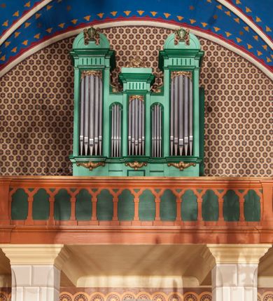 Zdjęcie nr 1: Szafa organowa architektoniczna, pięcioosiowa, jednokondygnacyjna, na wysokim cokole. Trzy główne osie u dołu podtrzymywane na ornamentalnych wspornikach, z prześwitami na piszczałki w formie stojącego prostokąta, ujętymi ramami, w górnej części dekorowane ornamentem roślinnym, zwieńczone fragmentami belkowania o fryzie dekorowanym żłobieniami. Oś środkowa niższa, zwieńczona szczytem z wolut podtrzymujących krzyż; osie skrajne najwyższe, zwieńczone szczytami w formie przerwanych półkolistych przyczółków z cokołami podtrzymującymi wazony pośrodku. Dwie środkowe osie najniższe z prześwitami na piszczałki w formie wydłużonego stojącego prostokąta zamkniętego łukiem półkolistym, ujęte ramami. Struktura polichromowana w kolorze jasnozielonym, z ciemnozielonymi profilami oraz złoconą ornamentyką. 