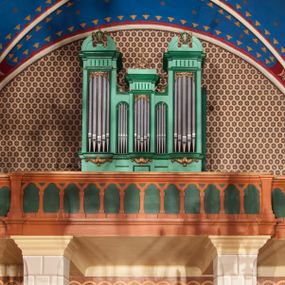 Zdjęcie nr 1: Szafa organowa architektoniczna, pięcioosiowa, jednokondygnacyjna, na wysokim cokole. Trzy główne osie u dołu podtrzymywane na ornamentalnych wspornikach, z prześwitami na piszczałki w formie stojącego prostokąta, ujętymi ramami, w górnej części dekorowane ornamentem roślinnym, zwieńczone fragmentami belkowania o fryzie dekorowanym żłobieniami. Oś środkowa niższa, zwieńczona szczytem z wolut podtrzymujących krzyż; osie skrajne najwyższe, zwieńczone szczytami w formie przerwanych półkolistych przyczółków z cokołami podtrzymującymi wazony pośrodku. Dwie środkowe osie najniższe z prześwitami na piszczałki w formie wydłużonego stojącego prostokąta zamkniętego łukiem półkolistym, ujęte ramami. Struktura polichromowana w kolorze jasnozielonym, z ciemnozielonymi profilami oraz złoconą ornamentyką. 