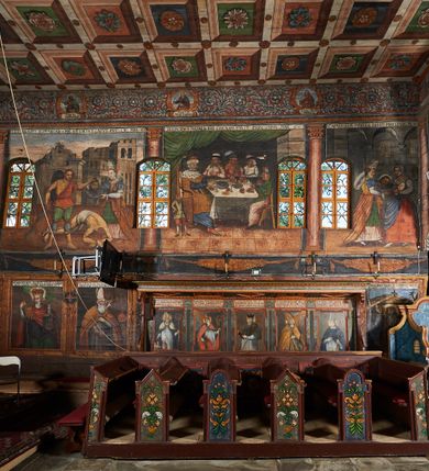 Zdjęcie nr 58: Polichromia ścienna prezbiterium pokrywa wszystkie ściany oraz strop tej części świątyni. 

Polichromia ścienna stropu
Strop zdobiony jest malowanymi kasetonami, w których umieszczone są rozety na różnokolorowych tłach. W centrum ukazane są dwie prostokątne kompozycje, ujęte w ornamentalne ramy. Od wschodu znajduje się Zwiastowanie Zachariaszowi, powyżej inskrypcja: „NE TIMEAS ZACHARIA VXOR TVA PARIET TIBI / FILIVM ET VOCABIS NOMEN EIVS IOANNEM LUCAE 1”. W drugiej kompozycji przedstawiono Nawiedzenie z Najświętszej Marii Panny ze św. Zachariaszem i św. Józefem, powyżej inskrypcja: „EXVLTAVIT IN GAVDIO INFANS IN VTERO MEO LUCAE 1”. 

Polichromia ścienna ścian prezbiterium
Dekoracje ścian o formie pasowej. W dolnej kondygnacji malowane iluzjonistycznie portrety świętych węgierskich w ornamentalnych ramach. Postacie ukazane do wysokości kolan, zwrócone trzy czwarte z odpowiednimi im atrybutami w dłoniach. Portrety opatrzone u góry łacińskimi opisami. Na ścianie północnej galerię otwiera wizerunek króla Stefana z napisem: „S(ANCTVS) STEPHANVS REX VNGARIAE, REGNVM SVVM DEIPARAE / DONAVIT OBIIT. 1038. 20 AVG(VSTVS) SEP. ALBERE 9.”. Następnie ukazani są kolejno: św. Emeryk „S(ANCTVS) EMERIGVS DVX VNGARIAE VT VIRGO MANERET, / A. CAELO PERSVASVS OBIIT. 1032. 5 nou. Sen. Albdvewas”, św. Władysław: „S(ANCTVS) LADISLAVS REX UNGARIAE ROSARIO ENSI OBVO/LUTO PVGNARE SOLITVS OBIIT 1097. 27.  iun. Sep. varad.”. Po drugiej stronie prezbiterium umieszczone są cztery obrazy świętych o tych samych wymiarach, również opatrzone napisami. Od lewej strony kolejno: św. Salomon „S(ANCTVS) SALOMON REX VNGARIAE DEIN EREMITA VITAE / AVSTERITATE FLORVIT OBIIT 1077. 28. Sept. Sep. Pold. in Idria”, św. Kazimierz: „S(ANCTVS) CASIMIRVS ELECTVS REX VNGARIAE AMORE / SARVANDAE VIRGINITATIS OBIIT 1484 4. MARTII.”, św. Dawid: „S(ANTCVS) DAVID REX SCOTIAE, FILIVS S(ANCTA) MARGA/RITAE VNGARA MATRE NATAE OBIIT 1153”, św. Ludwik: „S(SANCTVS) LVDOVICVS TOLOSANVS EP. E MARIA / REGIS VNG. FILIA NATVS OBIIT 1297 19 Aug(ustvs)”. Cykl ten kończy przy ścianie tęczowej przedstawienie św. Gintera „S(ANCVS) GVNTHERVS EREM. S(ANCTVS) STEPHANI REGIS / VNGARIAE COGNATVS OBIIT 1045 9. oct.”. Dodatkowo w obrazy wpisane są zacheuszki w formie równoramiennych krzyży ujętych w medaliony utworzone z wieńca. W zamknięciu prezbiterium przedstawienia diabłów, a od zachodu pod amboną czyściec.

Kondygnacja druga o podziałach architektonicznych u dołu wydzielona cokołem, dekorowanym złotymi girlandami na czarnym tle. Prostokątne pola wydzielone za pomocą malowanych iluzjonistycznie kolumn korynckich dźwigających architraw zdobiony stylizowanym kimationem jońskim. Powyżej fryz wypełniony wicią akantową, pomiędzy którą wplecione są kartusze z przedstawieniami świętych. W polach, pomiędzy kolumnami wielofigurowe kompozycje ze scenami z życia św. Jana Chrzciciela: Głos wołającego na pustyni „TV QVIS ES VOX CLAMANTIS IN DESERTO IOANN(IS) 1.”, Oto Baranek Boży „ECCE AGNVS DEI ECCE QVI TOLLIT PECCATVM MVNDI IOANN. IMÕ.”, Chrzest Jezusa w Jordanie „IESVS BAPTISTAVS EST A IONNE IN IORDANE MARCI. 1.”, Św. Jan Chrzciciel napomina Heroda „DICEBAT IOANNES HERODI NON LICET TIBI HABERE VXOREM FRATRIS TVI. MARCI 6,19.”, Św. Maria Magdalena pokutująca na pustyni, Św. Jan Chrzciciel na pustyni, Św. Jan Chrzciciel wtrącony do więzienia „HERODES TENVIT IONNEM ET VINXIT EVM IN CARCERE MAR 67o”, Kat podaje głowę św. Jana Chrzciciela Salome „DECOLLAVIT EVM IN CARCERE ET DEDIT CAPVT PVELLAE MAR.6.(?)”, Uczta Heroda „HERODES NATALIS SVI COENAM FECIT PRINCIPIBVS MAR. 6 10.”, Salome podaje głowę św. Jana Chrzciciela matce „CAPVT EIVS PVELLA DEDIT MATRI SVE M. 61”. 

W ostatniej, trzeciej strefie, umieszczonej w partii fryzu znajdują się medaliony. Na ścianie tęczowej, następnie na ścianie północnej i południowej ukazani są kolejno: św. Maciej „SA[N]CTVS / MATTHIAS”, Chrystus „IESVS / CHRISTVS”, św. Piotr „SANCTVS / PETRVS”, św. Szymon „SANCTVS / SIMON”, św. Andrzej „SANCTVS / ANDREAS”, św. Jakub Większy „S(ANCTVS) IACOBI / MAIORI”, św. Jan „(?)”, św. Filip „(?)”, św. Bartłomiej „SANCTVS / BARTHOLO/MAVS”, św. Tomasz „SANCTVS / THOMAS”, św. Mateusz „SANCTVS / MATTHAEVS”, św. Jakub Mniejszy „S(ANCTVS) IACOBVS / MINOR” i św. Juda Tadeusz „S(ANCVS) IVDA / THADEVS” na ścianie tęczowej od południa. Na belce tęczowej, od strony prezbiterium w wieńcu laurowym napis: „PICTVM / A[NNO] D[OMINI] 1711”.