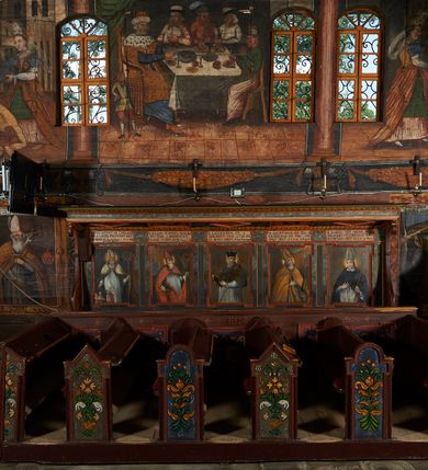 Zdjęcie nr 2: Polichromia ścienna prezbiterium pokrywa wszystkie ściany oraz strop tej części świątyni. 

Polichromia ścienna stropu
Strop zdobiony jest malowanymi kasetonami, w których umieszczone są rozety na różnokolorowych tłach. W centrum ukazane są dwie prostokątne kompozycje, ujęte w ornamentalne ramy. Od wschodu znajduje się Zwiastowanie Zachariaszowi, powyżej inskrypcja: „NE TIMEAS ZACHARIA VXOR TVA PARIET TIBI / FILIVM ET VOCABIS NOMEN EIVS IOANNEM LUCAE 1”. W drugiej kompozycji przedstawiono Nawiedzenie z Najświętszej Marii Panny ze św. Zachariaszem i św. Józefem, powyżej inskrypcja: „EXVLTAVIT IN GAVDIO INFANS IN VTERO MEO LUCAE 1”. 

Polichromia ścienna ścian prezbiterium
Dekoracje ścian o formie pasowej. W dolnej kondygnacji malowane iluzjonistycznie portrety świętych węgierskich w ornamentalnych ramach. Postacie ukazane do wysokości kolan, zwrócone trzy czwarte z odpowiednimi im atrybutami w dłoniach. Portrety opatrzone u góry łacińskimi opisami. Na ścianie północnej galerię otwiera wizerunek króla Stefana z napisem: „S(ANCTVS) STEPHANVS REX VNGARIAE, REGNVM SVVM DEIPARAE / DONAVIT OBIIT. 1038. 20 AVG(VSTVS) SEP. ALBERE 9.”. Następnie ukazani są kolejno: św. Emeryk „S(ANCTVS) EMERIGVS DVX VNGARIAE VT VIRGO MANERET, / A. CAELO PERSVASVS OBIIT. 1032. 5 nou. Sen. Albdvewas”, św. Władysław: „S(ANCTVS) LADISLAVS REX UNGARIAE ROSARIO ENSI OBVO/LUTO PVGNARE SOLITVS OBIIT 1097. 27.  iun. Sep. varad.”. Po drugiej stronie prezbiterium umieszczone są cztery obrazy świętych o tych samych wymiarach, również opatrzone napisami. Od lewej strony kolejno: św. Salomon „S(ANCTVS) SALOMON REX VNGARIAE DEIN EREMITA VITAE / AVSTERITATE FLORVIT OBIIT 1077. 28. Sept. Sep. Pold. in Idria”, św. Kazimierz: „S(ANCTVS) CASIMIRVS ELECTVS REX VNGARIAE AMORE / SARVANDAE VIRGINITATIS OBIIT 1484 4. MARTII.”, św. Dawid: „S(ANTCVS) DAVID REX SCOTIAE, FILIVS S(ANCTA) MARGA/RITAE VNGARA MATRE NATAE OBIIT 1153”, św. Ludwik: „S(SANCTVS) LVDOVICVS TOLOSANVS EP. E MARIA / REGIS VNG. FILIA NATVS OBIIT 1297 19 Aug(ustvs)”. Cykl ten kończy przy ścianie tęczowej przedstawienie św. Gintera „S(ANCVS) GVNTHERVS EREM. S(ANCTVS) STEPHANI REGIS / VNGARIAE COGNATVS OBIIT 1045 9. oct.”. Dodatkowo w obrazy wpisane są zacheuszki w formie równoramiennych krzyży ujętych w medaliony utworzone z wieńca. W zamknięciu prezbiterium przedstawienia diabłów, a od zachodu pod amboną czyściec.

Kondygnacja druga o podziałach architektonicznych u dołu wydzielona cokołem, dekorowanym złotymi girlandami na czarnym tle. Prostokątne pola wydzielone za pomocą malowanych iluzjonistycznie kolumn korynckich dźwigających architraw zdobiony stylizowanym kimationem jońskim. Powyżej fryz wypełniony wicią akantową, pomiędzy którą wplecione są kartusze z przedstawieniami świętych. W polach, pomiędzy kolumnami wielofigurowe kompozycje ze scenami z życia św. Jana Chrzciciela: Głos wołającego na pustyni „TV QVIS ES VOX CLAMANTIS IN DESERTO IOANN(IS) 1.”, Oto Baranek Boży „ECCE AGNVS DEI ECCE QVI TOLLIT PECCATVM MVNDI IOANN. IMÕ.”, Chrzest Jezusa w Jordanie „IESVS BAPTISTAVS EST A IONNE IN IORDANE MARCI. 1.”, Św. Jan Chrzciciel napomina Heroda „DICEBAT IOANNES HERODI NON LICET TIBI HABERE VXOREM FRATRIS TVI. MARCI 6,19.”, Św. Maria Magdalena pokutująca na pustyni, Św. Jan Chrzciciel na pustyni, Św. Jan Chrzciciel wtrącony do więzienia „HERODES TENVIT IONNEM ET VINXIT EVM IN CARCERE MAR 67o”, Kat podaje głowę św. Jana Chrzciciela Salome „DECOLLAVIT EVM IN CARCERE ET DEDIT CAPVT PVELLAE MAR.6.(?)”, Uczta Heroda „HERODES NATALIS SVI COENAM FECIT PRINCIPIBVS MAR. 6 10.”, Salome podaje głowę św. Jana Chrzciciela matce „CAPVT EIVS PVELLA DEDIT MATRI SVE M. 61”. 

W ostatniej, trzeciej strefie, umieszczonej w partii fryzu znajdują się medaliony. Na ścianie tęczowej, następnie na ścianie północnej i południowej ukazani są kolejno: św. Maciej „SA[N]CTVS / MATTHIAS”, Chrystus „IESVS / CHRISTVS”, św. Piotr „SANCTVS / PETRVS”, św. Szymon „SANCTVS / SIMON”, św. Andrzej „SANCTVS / ANDREAS”, św. Jakub Większy „S(ANCTVS) IACOBI / MAIORI”, św. Jan „(?)”, św. Filip „(?)”, św. Bartłomiej „SANCTVS / BARTHOLO/MAVS”, św. Tomasz „SANCTVS / THOMAS”, św. Mateusz „SANCTVS / MATTHAEVS”, św. Jakub Mniejszy „S(ANCTVS) IACOBVS / MINOR” i św. Juda Tadeusz „S(ANCVS) IVDA / THADEVS” na ścianie tęczowej od południa. Na belce tęczowej, od strony prezbiterium w wieńcu laurowym napis: „PICTVM / A[NNO] D[OMINI] 1711”.