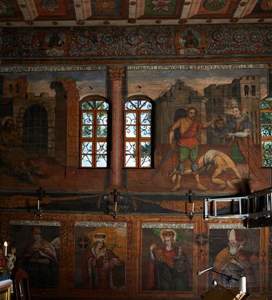 Zdjęcie nr 10: Polichromia ścienna prezbiterium pokrywa wszystkie ściany oraz strop tej części świątyni. 

Polichromia ścienna stropu
Strop zdobiony jest malowanymi kasetonami, w których umieszczone są rozety na różnokolorowych tłach. W centrum ukazane są dwie prostokątne kompozycje, ujęte w ornamentalne ramy. Od wschodu znajduje się Zwiastowanie Zachariaszowi, powyżej inskrypcja: „NE TIMEAS ZACHARIA VXOR TVA PARIET TIBI / FILIVM ET VOCABIS NOMEN EIVS IOANNEM LUCAE 1”. W drugiej kompozycji przedstawiono Nawiedzenie z Najświętszej Marii Panny ze św. Zachariaszem i św. Józefem, powyżej inskrypcja: „EXVLTAVIT IN GAVDIO INFANS IN VTERO MEO LUCAE 1”. 

Polichromia ścienna ścian prezbiterium
Dekoracje ścian o formie pasowej. W dolnej kondygnacji malowane iluzjonistycznie portrety świętych węgierskich w ornamentalnych ramach. Postacie ukazane do wysokości kolan, zwrócone trzy czwarte z odpowiednimi im atrybutami w dłoniach. Portrety opatrzone u góry łacińskimi opisami. Na ścianie północnej galerię otwiera wizerunek króla Stefana z napisem: „S(ANCTVS) STEPHANVS REX VNGARIAE, REGNVM SVVM DEIPARAE / DONAVIT OBIIT. 1038. 20 AVG(VSTVS) SEP. ALBERE 9.”. Następnie ukazani są kolejno: św. Emeryk „S(ANCTVS) EMERIGVS DVX VNGARIAE VT VIRGO MANERET, / A. CAELO PERSVASVS OBIIT. 1032. 5 nou. Sen. Albdvewas”, św. Władysław: „S(ANCTVS) LADISLAVS REX UNGARIAE ROSARIO ENSI OBVO/LUTO PVGNARE SOLITVS OBIIT 1097. 27.  iun. Sep. varad.”. Po drugiej stronie prezbiterium umieszczone są cztery obrazy świętych o tych samych wymiarach, również opatrzone napisami. Od lewej strony kolejno: św. Salomon „S(ANCTVS) SALOMON REX VNGARIAE DEIN EREMITA VITAE / AVSTERITATE FLORVIT OBIIT 1077. 28. Sept. Sep. Pold. in Idria”, św. Kazimierz: „S(ANCTVS) CASIMIRVS ELECTVS REX VNGARIAE AMORE / SARVANDAE VIRGINITATIS OBIIT 1484 4. MARTII.”, św. Dawid: „S(ANTCVS) DAVID REX SCOTIAE, FILIVS S(ANCTA) MARGA/RITAE VNGARA MATRE NATAE OBIIT 1153”, św. Ludwik: „S(SANCTVS) LVDOVICVS TOLOSANVS EP. E MARIA / REGIS VNG. FILIA NATVS OBIIT 1297 19 Aug(ustvs)”. Cykl ten kończy przy ścianie tęczowej przedstawienie św. Gintera „S(ANCVS) GVNTHERVS EREM. S(ANCTVS) STEPHANI REGIS / VNGARIAE COGNATVS OBIIT 1045 9. oct.”. Dodatkowo w obrazy wpisane są zacheuszki w formie równoramiennych krzyży ujętych w medaliony utworzone z wieńca. W zamknięciu prezbiterium przedstawienia diabłów, a od zachodu pod amboną czyściec.

Kondygnacja druga o podziałach architektonicznych u dołu wydzielona cokołem, dekorowanym złotymi girlandami na czarnym tle. Prostokątne pola wydzielone za pomocą malowanych iluzjonistycznie kolumn korynckich dźwigających architraw zdobiony stylizowanym kimationem jońskim. Powyżej fryz wypełniony wicią akantową, pomiędzy którą wplecione są kartusze z przedstawieniami świętych. W polach, pomiędzy kolumnami wielofigurowe kompozycje ze scenami z życia św. Jana Chrzciciela: Głos wołającego na pustyni „TV QVIS ES VOX CLAMANTIS IN DESERTO IOANN(IS) 1.”, Oto Baranek Boży „ECCE AGNVS DEI ECCE QVI TOLLIT PECCATVM MVNDI IOANN. IMÕ.”, Chrzest Jezusa w Jordanie „IESVS BAPTISTAVS EST A IONNE IN IORDANE MARCI. 1.”, Św. Jan Chrzciciel napomina Heroda „DICEBAT IOANNES HERODI NON LICET TIBI HABERE VXOREM FRATRIS TVI. MARCI 6,19.”, Św. Maria Magdalena pokutująca na pustyni, Św. Jan Chrzciciel na pustyni, Św. Jan Chrzciciel wtrącony do więzienia „HERODES TENVIT IONNEM ET VINXIT EVM IN CARCERE MAR 67o”, Kat podaje głowę św. Jana Chrzciciela Salome „DECOLLAVIT EVM IN CARCERE ET DEDIT CAPVT PVELLAE MAR.6.(?)”, Uczta Heroda „HERODES NATALIS SVI COENAM FECIT PRINCIPIBVS MAR. 6 10.”, Salome podaje głowę św. Jana Chrzciciela matce „CAPVT EIVS PVELLA DEDIT MATRI SVE M. 61”. 

W ostatniej, trzeciej strefie, umieszczonej w partii fryzu znajdują się medaliony. Na ścianie tęczowej, następnie na ścianie północnej i południowej ukazani są kolejno: św. Maciej „SA[N]CTVS / MATTHIAS”, Chrystus „IESVS / CHRISTVS”, św. Piotr „SANCTVS / PETRVS”, św. Szymon „SANCTVS / SIMON”, św. Andrzej „SANCTVS / ANDREAS”, św. Jakub Większy „S(ANCTVS) IACOBI / MAIORI”, św. Jan „(?)”, św. Filip „(?)”, św. Bartłomiej „SANCTVS / BARTHOLO/MAVS”, św. Tomasz „SANCTVS / THOMAS”, św. Mateusz „SANCTVS / MATTHAEVS”, św. Jakub Mniejszy „S(ANCTVS) IACOBVS / MINOR” i św. Juda Tadeusz „S(ANCVS) IVDA / THADEVS” na ścianie tęczowej od południa. Na belce tęczowej, od strony prezbiterium w wieńcu laurowym napis: „PICTVM / A[NNO] D[OMINI] 1711”.