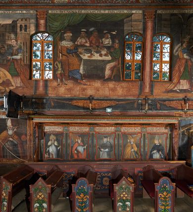 Zdjęcie nr 9: Polichromia ścienna prezbiterium pokrywa wszystkie ściany oraz strop tej części świątyni. 

Polichromia ścienna stropu
Strop zdobiony jest malowanymi kasetonami, w których umieszczone są rozety na różnokolorowych tłach. W centrum ukazane są dwie prostokątne kompozycje, ujęte w ornamentalne ramy. Od wschodu znajduje się Zwiastowanie Zachariaszowi, powyżej inskrypcja: „NE TIMEAS ZACHARIA VXOR TVA PARIET TIBI / FILIVM ET VOCABIS NOMEN EIVS IOANNEM LUCAE 1”. W drugiej kompozycji przedstawiono Nawiedzenie z Najświętszej Marii Panny ze św. Zachariaszem i św. Józefem, powyżej inskrypcja: „EXVLTAVIT IN GAVDIO INFANS IN VTERO MEO LUCAE 1”. 

Polichromia ścienna ścian prezbiterium
Dekoracje ścian o formie pasowej. W dolnej kondygnacji malowane iluzjonistycznie portrety świętych węgierskich w ornamentalnych ramach. Postacie ukazane do wysokości kolan, zwrócone trzy czwarte z odpowiednimi im atrybutami w dłoniach. Portrety opatrzone u góry łacińskimi opisami. Na ścianie północnej galerię otwiera wizerunek króla Stefana z napisem: „S(ANCTVS) STEPHANVS REX VNGARIAE, REGNVM SVVM DEIPARAE / DONAVIT OBIIT. 1038. 20 AVG(VSTVS) SEP. ALBERE 9.”. Następnie ukazani są kolejno: św. Emeryk „S(ANCTVS) EMERIGVS DVX VNGARIAE VT VIRGO MANERET, / A. CAELO PERSVASVS OBIIT. 1032. 5 nou. Sen. Albdvewas”, św. Władysław: „S(ANCTVS) LADISLAVS REX UNGARIAE ROSARIO ENSI OBVO/LUTO PVGNARE SOLITVS OBIIT 1097. 27.  iun. Sep. varad.”. Po drugiej stronie prezbiterium umieszczone są cztery obrazy świętych o tych samych wymiarach, również opatrzone napisami. Od lewej strony kolejno: św. Salomon „S(ANCTVS) SALOMON REX VNGARIAE DEIN EREMITA VITAE / AVSTERITATE FLORVIT OBIIT 1077. 28. Sept. Sep. Pold. in Idria”, św. Kazimierz: „S(ANCTVS) CASIMIRVS ELECTVS REX VNGARIAE AMORE / SARVANDAE VIRGINITATIS OBIIT 1484 4. MARTII.”, św. Dawid: „S(ANTCVS) DAVID REX SCOTIAE, FILIVS S(ANCTA) MARGA/RITAE VNGARA MATRE NATAE OBIIT 1153”, św. Ludwik: „S(SANCTVS) LVDOVICVS TOLOSANVS EP. E MARIA / REGIS VNG. FILIA NATVS OBIIT 1297 19 Aug(ustvs)”. Cykl ten kończy przy ścianie tęczowej przedstawienie św. Gintera „S(ANCVS) GVNTHERVS EREM. S(ANCTVS) STEPHANI REGIS / VNGARIAE COGNATVS OBIIT 1045 9. oct.”. Dodatkowo w obrazy wpisane są zacheuszki w formie równoramiennych krzyży ujętych w medaliony utworzone z wieńca. W zamknięciu prezbiterium przedstawienia diabłów, a od zachodu pod amboną czyściec.

Kondygnacja druga o podziałach architektonicznych u dołu wydzielona cokołem, dekorowanym złotymi girlandami na czarnym tle. Prostokątne pola wydzielone za pomocą malowanych iluzjonistycznie kolumn korynckich dźwigających architraw zdobiony stylizowanym kimationem jońskim. Powyżej fryz wypełniony wicią akantową, pomiędzy którą wplecione są kartusze z przedstawieniami świętych. W polach, pomiędzy kolumnami wielofigurowe kompozycje ze scenami z życia św. Jana Chrzciciela: Głos wołającego na pustyni „TV QVIS ES VOX CLAMANTIS IN DESERTO IOANN(IS) 1.”, Oto Baranek Boży „ECCE AGNVS DEI ECCE QVI TOLLIT PECCATVM MVNDI IOANN. IMÕ.”, Chrzest Jezusa w Jordanie „IESVS BAPTISTAVS EST A IONNE IN IORDANE MARCI. 1.”, Św. Jan Chrzciciel napomina Heroda „DICEBAT IOANNES HERODI NON LICET TIBI HABERE VXOREM FRATRIS TVI. MARCI 6,19.”, Św. Maria Magdalena pokutująca na pustyni, Św. Jan Chrzciciel na pustyni, Św. Jan Chrzciciel wtrącony do więzienia „HERODES TENVIT IONNEM ET VINXIT EVM IN CARCERE MAR 67o”, Kat podaje głowę św. Jana Chrzciciela Salome „DECOLLAVIT EVM IN CARCERE ET DEDIT CAPVT PVELLAE MAR.6.(?)”, Uczta Heroda „HERODES NATALIS SVI COENAM FECIT PRINCIPIBVS MAR. 6 10.”, Salome podaje głowę św. Jana Chrzciciela matce „CAPVT EIVS PVELLA DEDIT MATRI SVE M. 61”. 

W ostatniej, trzeciej strefie, umieszczonej w partii fryzu znajdują się medaliony. Na ścianie tęczowej, następnie na ścianie północnej i południowej ukazani są kolejno: św. Maciej „SA[N]CTVS / MATTHIAS”, Chrystus „IESVS / CHRISTVS”, św. Piotr „SANCTVS / PETRVS”, św. Szymon „SANCTVS / SIMON”, św. Andrzej „SANCTVS / ANDREAS”, św. Jakub Większy „S(ANCTVS) IACOBI / MAIORI”, św. Jan „(?)”, św. Filip „(?)”, św. Bartłomiej „SANCTVS / BARTHOLO/MAVS”, św. Tomasz „SANCTVS / THOMAS”, św. Mateusz „SANCTVS / MATTHAEVS”, św. Jakub Mniejszy „S(ANCTVS) IACOBVS / MINOR” i św. Juda Tadeusz „S(ANCVS) IVDA / THADEVS” na ścianie tęczowej od południa. Na belce tęczowej, od strony prezbiterium w wieńcu laurowym napis: „PICTVM / A[NNO] D[OMINI] 1711”.