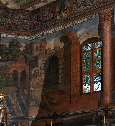 Zdjęcie nr 12: Polichromia ścienna prezbiterium pokrywa wszystkie ściany oraz strop tej części świątyni. 

Polichromia ścienna stropu
Strop zdobiony jest malowanymi kasetonami, w których umieszczone są rozety na różnokolorowych tłach. W centrum ukazane są dwie prostokątne kompozycje, ujęte w ornamentalne ramy. Od wschodu znajduje się Zwiastowanie Zachariaszowi, powyżej inskrypcja: „NE TIMEAS ZACHARIA VXOR TVA PARIET TIBI / FILIVM ET VOCABIS NOMEN EIVS IOANNEM LUCAE 1”. W drugiej kompozycji przedstawiono Nawiedzenie z Najświętszej Marii Panny ze św. Zachariaszem i św. Józefem, powyżej inskrypcja: „EXVLTAVIT IN GAVDIO INFANS IN VTERO MEO LUCAE 1”. 

Polichromia ścienna ścian prezbiterium
Dekoracje ścian o formie pasowej. W dolnej kondygnacji malowane iluzjonistycznie portrety świętych węgierskich w ornamentalnych ramach. Postacie ukazane do wysokości kolan, zwrócone trzy czwarte z odpowiednimi im atrybutami w dłoniach. Portrety opatrzone u góry łacińskimi opisami. Na ścianie północnej galerię otwiera wizerunek króla Stefana z napisem: „S(ANCTVS) STEPHANVS REX VNGARIAE, REGNVM SVVM DEIPARAE / DONAVIT OBIIT. 1038. 20 AVG(VSTVS) SEP. ALBERE 9.”. Następnie ukazani są kolejno: św. Emeryk „S(ANCTVS) EMERIGVS DVX VNGARIAE VT VIRGO MANERET, / A. CAELO PERSVASVS OBIIT. 1032. 5 nou. Sen. Albdvewas”, św. Władysław: „S(ANCTVS) LADISLAVS REX UNGARIAE ROSARIO ENSI OBVO/LUTO PVGNARE SOLITVS OBIIT 1097. 27.  iun. Sep. varad.”. Po drugiej stronie prezbiterium umieszczone są cztery obrazy świętych o tych samych wymiarach, również opatrzone napisami. Od lewej strony kolejno: św. Salomon „S(ANCTVS) SALOMON REX VNGARIAE DEIN EREMITA VITAE / AVSTERITATE FLORVIT OBIIT 1077. 28. Sept. Sep. Pold. in Idria”, św. Kazimierz: „S(ANCTVS) CASIMIRVS ELECTVS REX VNGARIAE AMORE / SARVANDAE VIRGINITATIS OBIIT 1484 4. MARTII.”, św. Dawid: „S(ANTCVS) DAVID REX SCOTIAE, FILIVS S(ANCTA) MARGA/RITAE VNGARA MATRE NATAE OBIIT 1153”, św. Ludwik: „S(SANCTVS) LVDOVICVS TOLOSANVS EP. E MARIA / REGIS VNG. FILIA NATVS OBIIT 1297 19 Aug(ustvs)”. Cykl ten kończy przy ścianie tęczowej przedstawienie św. Gintera „S(ANCVS) GVNTHERVS EREM. S(ANCTVS) STEPHANI REGIS / VNGARIAE COGNATVS OBIIT 1045 9. oct.”. Dodatkowo w obrazy wpisane są zacheuszki w formie równoramiennych krzyży ujętych w medaliony utworzone z wieńca. W zamknięciu prezbiterium przedstawienia diabłów, a od zachodu pod amboną czyściec.

Kondygnacja druga o podziałach architektonicznych u dołu wydzielona cokołem, dekorowanym złotymi girlandami na czarnym tle. Prostokątne pola wydzielone za pomocą malowanych iluzjonistycznie kolumn korynckich dźwigających architraw zdobiony stylizowanym kimationem jońskim. Powyżej fryz wypełniony wicią akantową, pomiędzy którą wplecione są kartusze z przedstawieniami świętych. W polach, pomiędzy kolumnami wielofigurowe kompozycje ze scenami z życia św. Jana Chrzciciela: Głos wołającego na pustyni „TV QVIS ES VOX CLAMANTIS IN DESERTO IOANN(IS) 1.”, Oto Baranek Boży „ECCE AGNVS DEI ECCE QVI TOLLIT PECCATVM MVNDI IOANN. IMÕ.”, Chrzest Jezusa w Jordanie „IESVS BAPTISTAVS EST A IONNE IN IORDANE MARCI. 1.”, Św. Jan Chrzciciel napomina Heroda „DICEBAT IOANNES HERODI NON LICET TIBI HABERE VXOREM FRATRIS TVI. MARCI 6,19.”, Św. Maria Magdalena pokutująca na pustyni, Św. Jan Chrzciciel na pustyni, Św. Jan Chrzciciel wtrącony do więzienia „HERODES TENVIT IONNEM ET VINXIT EVM IN CARCERE MAR 67o”, Kat podaje głowę św. Jana Chrzciciela Salome „DECOLLAVIT EVM IN CARCERE ET DEDIT CAPVT PVELLAE MAR.6.(?)”, Uczta Heroda „HERODES NATALIS SVI COENAM FECIT PRINCIPIBVS MAR. 6 10.”, Salome podaje głowę św. Jana Chrzciciela matce „CAPVT EIVS PVELLA DEDIT MATRI SVE M. 61”. 

W ostatniej, trzeciej strefie, umieszczonej w partii fryzu znajdują się medaliony. Na ścianie tęczowej, następnie na ścianie północnej i południowej ukazani są kolejno: św. Maciej „SA[N]CTVS / MATTHIAS”, Chrystus „IESVS / CHRISTVS”, św. Piotr „SANCTVS / PETRVS”, św. Szymon „SANCTVS / SIMON”, św. Andrzej „SANCTVS / ANDREAS”, św. Jakub Większy „S(ANCTVS) IACOBI / MAIORI”, św. Jan „(?)”, św. Filip „(?)”, św. Bartłomiej „SANCTVS / BARTHOLO/MAVS”, św. Tomasz „SANCTVS / THOMAS”, św. Mateusz „SANCTVS / MATTHAEVS”, św. Jakub Mniejszy „S(ANCTVS) IACOBVS / MINOR” i św. Juda Tadeusz „S(ANCVS) IVDA / THADEVS” na ścianie tęczowej od południa. Na belce tęczowej, od strony prezbiterium w wieńcu laurowym napis: „PICTVM / A[NNO] D[OMINI] 1711”.