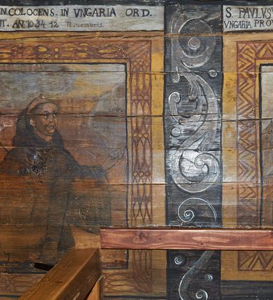 Zdjęcie nr 34: Polichromia ścienna nawy pokrywa wszystkie ściany oraz strop tej części świątyni. Polichromia figuralno-ornamentalna. W łuku tęczowym fryz podstropowy, wypełniony ornamentem w formie schematycznej, stylizowanej wici roślinnej, ujętej na krańcach uskrzydlonymi główkami anielskimi, umieszczonymi w medalionach. Poniżej fryzu, po lewej herb cesarski, ujęty w wieniec laurowy, w tle pejzaż; po przeciwnej stronie, zwieńczony insygniami biskupimi, herb biskupa Jerzego Lippay de Zongor – dwa lwy, ustawione antytetycznie przy ukoronowanej kolumnie.

Na północnej ścianie nawy do wysokości jednej trzeciej ściany pas kwater z wizerunkami świętych, ujętymi w obramienia, utworzone z ornamentu w formie silnie stylizowanej wici roślinnej. Pola pomiędzy kwaterami wypełnione schematycznym ornamentem geometryczno-figuralnym, złożonym ze skręconej wici roślinnej oraz główek anielskich. Od strony prezbiterium kolejno przedstawienia opatrzone następującymi podpisami:
„S(NCTVS) ADREAS ZOREARBUS EREMITA NITRAE / ET TRENCHINII  27 XIV LY ANNO 1609”;
„B. MATHEAI ESCANDELI NATUS BUDAE MARTIRIO AFFE/CTUS in Sinis quo infide infidelum convertendorum causa penefravit”;
„B. SADOCH ORD. PRAED. A. S. DOMINICO in UNGARIAM/ MISSUS EGREGIE LABORAVIT MARTYRIO  affectus 1260. 3. Iunii”;
„S(ANCTVS) COLOMANUS MS. MARGARITAE REGINAE SCOTIAE UNGARA/ MATRE NATAE FILIUS SUSPENSUS STOKARAVIAE COLIT 13 oct.”;
„S(ANCTVS) CAPISTRANI ORD. S. FRAC. TURCAS BELRADO FUGAVIT/ UNG. Ufilissim[us] obit 1455 23 Od. Viilaci in Ung. Sepult[us].”;
„S(ANCTVS) PETRUS THOMASIUS CARMELITA AT LUDOVICUM/ UNG. REGEM NUNTI[US] APOSTOL. De pace cum Venetis egit obit 29 9 1367”.

Kontynuacja przedstawień na ścianie zachodniej:
„B. IACOBUS PICENUS ORD. S. FRANC. S. CAPISTRANI IN UNG./ COAPOSTOL[US] MULTOS AD CHRISTI FIDEM CONVERTIT”;
„S(ANCTVS) IOANNES NEPOMUCN.”.

W górnej partii ściany północnej scena wielofiguralna: Św. Jan Chrzciciel nauczający w otoczeniu tłumu. W tle pejzaż z drzewami i  zarysowanym na najdalszym planie masywem górskim. Ponad przedstawieniem napis: „VENIT IN OMNEM REGIONEM PRAEDICANS BAPTISMUM POENITENITIAE LUCAE 3.”. Do sceny kazania św Jana Chrzciciela przylega środkowy rząd wizerunków świętych. Cztery pierwsze przedstawienia znajdują się na ścianie północnej i biegną w kierunku chóru muzycznego:
„B. BERTHODEUS (…) 17 DECE”;
„B. IOANNES DOMINICI ORD. PRAED. EP. Et. CARDIN ad. SIGISMUN. UN. BEC. NUNT. APOTOLIC. BUDAE obiit (…) 1418” [w lewym górnym rogu odnotowane białą farbą informacje o kolejnych konserwacjach polichromii];
„B. ANTONIUS UNGARUS ORD. FRANC. FULGINII/IN OBSEQUIO INFIRMORUM ob. 1398. 13 May.”;
„B. MATHAEUS ESCANDELI NATUS BUDA MARTIRIS AFFECTUS IN SINIS QUO INFIDELIUM…”.

Nad chórem muzycznym, na ścianie zachodniej znajdują się kolejne cztery wizerunki z tego cyklu:
„B. MURITIUS CSAKY ORD. PRAED AMORE IN DEIPURAM MIRACU/LIS CLARUS obiit laurmi 1336 20. Mar. [.]oii Ferr.”;
„B. MAURUS EX MANASTETRIO S. MARTINI /ORD. S. BENED. EPISC. QUINQUE ECCLESIENS in UNGARIA”;
„S(ANCTVS) BENEDICTUS MAR. EREMITA PROPE TRENCHINIUM/IN VASUM MERSUS COLITUR IM aii”;
„B. EUSEBIUS CANONICO STRIGOMI PRIMUS/PROVINCIALIS ORA: S. PAULI primi Erem: obit 1270. 20. Ian.”.

Ostatnie dwa wizerunki na ścianie południowej nad chórem muzycznym, kolejno od strony ściany tęczowej:
„S(ANCTVS) ASTRICQ ARCHIEN. COLOCENS. IN UNGARIA ORD./ s. BENEDICTI OBIIT. AN. 1034. 12 Novembris”;
„S(ANCTVS) PAULUS UNGARUS PRIMUS ORD. PRAED./ UNGARIA PROVINCIALIS MARTIRIO affectis”.

Na podniebiu zaskrzynienia kontynuacja cyklu hagiograficznego. Od łuku tęczowego, wizerunki umieszczone są między elementami ornamentacyjnym, opatrzone następującymi podpisami:
„B. GISELA S. STEPH. R. / U. CONIUX Ob. 1036”;
„S(ANCTVS) ESABETH ANDR. U. FI/LIA DUCISS THURINN ob. 1226”;
„B. GERTRUDIS V. FILIA/ S. ELISABETHAE THURING”;
„B. ELISABETH HELVETA AN/ DR III R.U. FILIA ob. 1338 6 mai”;
„B. HELENA V. ORD. PRAEDIC. OB. BUD. AN. 1720 9 nov.”;
„S(ANCTVS) MARGHARITA REGINA SCOTIAE NATA IN UNGARIA TEMORAE S. SALAMONIS”;
„B. ELISABETHU. Ord. Praed S. STEPHANI UNG. REGIS. FILIA OBIIT CIV. Anno 1285 6 martii”;
„S(ANCTA) URSULA CUM 11 000 VIRGINUM AB ATTILA INTERFECTA 1383 21 Oct.”.

Na podniebiu zaskrzynienia nad ścianą południową kontynuacja cyklu, od tęczy:
„B. MARGARITA FILIA BELAE 4 R. V. Ob. 1273. 28 Ian.”; 
„B. CUNEGUNDUDIS V. BELAE IV REG FILIA Ob. 1292. 24. 1.”.

Na ścianie południowej w dolnym pasie malowideł od strony tęczy scena figuralna z przedstawieniem św. Anny nauczającej Marię, a następnie scena piekła z przedstawieniem męki grzeszników w wypełnionej płomieniami paszczy Lewiatana. W górnej partii scena przedstawiająca pogrzeb Jana Chrzciciela. Przestrzenie wokół tego malowidła i okien szczelnie wypełnione ornamentem w formie schematycznej wici roślinnej. Drzwi pokryte dekoracją ornamentalną analogiczną do tej w przestrzeniach między obrazami w dolnym rzędzie cyklu świętych na ścianie północnej. Fryz przystropowy w całości dekorowany analogicznie jak w łuku tęczowym. 

Na stropie kontynuacja cyklu ze scenami z życia Jana Chrzciciela, rozpoczynającego się w prezbiterium. Dwa obrazy w formie prostokątów, ujęte w malowane ramy, utworzone z ornamentu złożonego z wici roślinnej i stylizowanych rozetek. Pierwsza od tęczy wielopostaciowa scena narodzin Jana Chrzciciela, w górnej partii opatrzona napisem: „QUIS PUTAS PUER ISTE ERITE IOANNES EST NOMEN EIUS LUCAE 1.”. Bliżej chóru przedstawienie Jana Chrzciciela, nauczającego na puszczy, opatrzona podpisem: „ERAT IN DESERTIS USQUE IN DIEM OSTENSIONIS SUAE LUCAE 1.”. Obrazy ujęte w iluzjonistycznie malowane kasetony z rozetami w środku. Podziały kasetonowe zaznaczone listewkami, dekorowanymi rozetkami. Pod amboną niewielkich rozmiarów malowidło, przedstawiające siedem postaci pokutujących w czyśćcu i anioła. Scena zwieńczona monogramem IHS.
