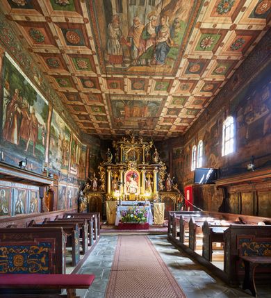 Zdjęcie nr 12: Kościół św. Jana Chrzciciela w Orawce usytuowany jest w centrum wsi na zachód od drogi prowadzącej z Jabłonki do Podwilka. Jest otoczony starodrzewiem, teren przykościelny opasany jest murem z łamanego kamienia. W granicach ogrodzenia znajduje się rozległy cmentarz przykościelny. 

Kościół orientowany, drewniany, konstrukcji zrębowej z wieżą na słup na kamiennej podmurówce. Prezbiterium wydłużone i zamknięte wielobocznie, nawa szersza i prostokątna. Przy prezbiterium od północy usytuowana jest zakrystia, a od wschodu murowana kaplica Matki Boskiej Bolesnej z 1728 roku o wielobocznym zakończeniu z przybudówką w rodzaju zakrystii od północy. Świątynia zbudowana jest z bierwion, łączonych na kwadratowy czop, bez ostatków. Poszczególne barwiona umocnione są pionowo tyblami. 

Wnętrze kościoła nakrywają stropy drewniane, płaskie, w nawie z zaskrzynieniami, podpartymi słupami. Zaskrzynienia w nawie obite są deskami dekorowanymi polichromią. W kaplicy Matki Boskiej Bolesnej sklepienie kolebkowe z lunetami. Ściana arkady tęczowej zamknięta jest łukiem półkolistym, na belce tęczowej umieszczona jest Grupa Ukrzyżowania. Przy nawie od południa dobudowana jest nowsza, drewniana kruchta. Chór muzyczny wsparty na dwóch profilowanych słupach z nim złączony chórek boczny przy północnej ścianie nawy. Otwory okienne usytuowane wyłącznie od strony południowej w kształcie stojących prostokątów, zamknięte półkoliście.

Na zewnątrz ściany świątyni obite gontem z wyjątkiem murowanej kaplicy Matki Boskiej Bolesnej, która została otynkowana. Wieża częściowo wtopiona w korpus, częściowo wysunięta ryzalitycznie; w przyziemiu babiniec. Wieża wzniesiona w konstrukcji słupowo-ramowej, główne narożne słupy nośne pochylone, wzmocnione tzw. krzyżami św. Andrzeja. Wieża zwieńczona jest nadwieszoną izbicą, szalowaną deskami w układzie pionowym z listwowaniem z czterolistnymi okienkami. Wyżej ostrosłupowy hełm z czterema narożnymi wieżyczkami. Kościół nakryty gontem w postaci długiego, kalenicowego dachu o rozległych połaciach, otulonym płaszczem gontowym z szerokim, załamanym okapem. Na wspólnym dachu kościoła i kaplicy nowa wieżyczka na sygnaturkę. 