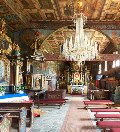 Zdjęcie nr 13: Kościół św. Jana Chrzciciela w Orawce usytuowany jest w centrum wsi na zachód od drogi prowadzącej z Jabłonki do Podwilka. Jest otoczony starodrzewiem, teren przykościelny opasany jest murem z łamanego kamienia. W granicach ogrodzenia znajduje się rozległy cmentarz przykościelny. 

Kościół orientowany, drewniany, konstrukcji zrębowej z wieżą na słup na kamiennej podmurówce. Prezbiterium wydłużone i zamknięte wielobocznie, nawa szersza i prostokątna. Przy prezbiterium od północy usytuowana jest zakrystia, a od wschodu murowana kaplica Matki Boskiej Bolesnej z 1728 roku o wielobocznym zakończeniu z przybudówką w rodzaju zakrystii od północy. Świątynia zbudowana jest z bierwion, łączonych na kwadratowy czop, bez ostatków. Poszczególne barwiona umocnione są pionowo tyblami. 

Wnętrze kościoła nakrywają stropy drewniane, płaskie, w nawie z zaskrzynieniami, podpartymi słupami. Zaskrzynienia w nawie obite są deskami dekorowanymi polichromią. W kaplicy Matki Boskiej Bolesnej sklepienie kolebkowe z lunetami. Ściana arkady tęczowej zamknięta jest łukiem półkolistym, na belce tęczowej umieszczona jest Grupa Ukrzyżowania. Przy nawie od południa dobudowana jest nowsza, drewniana kruchta. Chór muzyczny wsparty na dwóch profilowanych słupach z nim złączony chórek boczny przy północnej ścianie nawy. Otwory okienne usytuowane wyłącznie od strony południowej w kształcie stojących prostokątów, zamknięte półkoliście.

Na zewnątrz ściany świątyni obite gontem z wyjątkiem murowanej kaplicy Matki Boskiej Bolesnej, która została otynkowana. Wieża częściowo wtopiona w korpus, częściowo wysunięta ryzalitycznie; w przyziemiu babiniec. Wieża wzniesiona w konstrukcji słupowo-ramowej, główne narożne słupy nośne pochylone, wzmocnione tzw. krzyżami św. Andrzeja. Wieża zwieńczona jest nadwieszoną izbicą, szalowaną deskami w układzie pionowym z listwowaniem z czterolistnymi okienkami. Wyżej ostrosłupowy hełm z czterema narożnymi wieżyczkami. Kościół nakryty gontem w postaci długiego, kalenicowego dachu o rozległych połaciach, otulonym płaszczem gontowym z szerokim, załamanym okapem. Na wspólnym dachu kościoła i kaplicy nowa wieżyczka na sygnaturkę. 