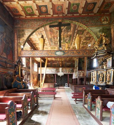 Zdjęcie nr 18: Kościół św. Jana Chrzciciela w Orawce usytuowany jest w centrum wsi na zachód od drogi prowadzącej z Jabłonki do Podwilka. Jest otoczony starodrzewiem, teren przykościelny opasany jest murem z łamanego kamienia. W granicach ogrodzenia znajduje się rozległy cmentarz przykościelny. 

Kościół orientowany, drewniany, konstrukcji zrębowej z wieżą na słup na kamiennej podmurówce. Prezbiterium wydłużone i zamknięte wielobocznie, nawa szersza i prostokątna. Przy prezbiterium od północy usytuowana jest zakrystia, a od wschodu murowana kaplica Matki Boskiej Bolesnej z 1728 roku o wielobocznym zakończeniu z przybudówką w rodzaju zakrystii od północy. Świątynia zbudowana jest z bierwion, łączonych na kwadratowy czop, bez ostatków. Poszczególne barwiona umocnione są pionowo tyblami. 

Wnętrze kościoła nakrywają stropy drewniane, płaskie, w nawie z zaskrzynieniami, podpartymi słupami. Zaskrzynienia w nawie obite są deskami dekorowanymi polichromią. W kaplicy Matki Boskiej Bolesnej sklepienie kolebkowe z lunetami. Ściana arkady tęczowej zamknięta jest łukiem półkolistym, na belce tęczowej umieszczona jest Grupa Ukrzyżowania. Przy nawie od południa dobudowana jest nowsza, drewniana kruchta. Chór muzyczny wsparty na dwóch profilowanych słupach z nim złączony chórek boczny przy północnej ścianie nawy. Otwory okienne usytuowane wyłącznie od strony południowej w kształcie stojących prostokątów, zamknięte półkoliście.

Na zewnątrz ściany świątyni obite gontem z wyjątkiem murowanej kaplicy Matki Boskiej Bolesnej, która została otynkowana. Wieża częściowo wtopiona w korpus, częściowo wysunięta ryzalitycznie; w przyziemiu babiniec. Wieża wzniesiona w konstrukcji słupowo-ramowej, główne narożne słupy nośne pochylone, wzmocnione tzw. krzyżami św. Andrzeja. Wieża zwieńczona jest nadwieszoną izbicą, szalowaną deskami w układzie pionowym z listwowaniem z czterolistnymi okienkami. Wyżej ostrosłupowy hełm z czterema narożnymi wieżyczkami. Kościół nakryty gontem w postaci długiego, kalenicowego dachu o rozległych połaciach, otulonym płaszczem gontowym z szerokim, załamanym okapem. Na wspólnym dachu kościoła i kaplicy nowa wieżyczka na sygnaturkę. 