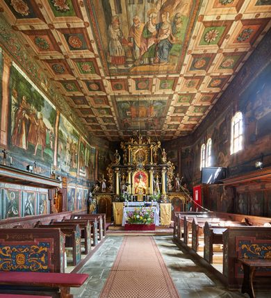 Zdjęcie nr 14: Kościół św. Jana Chrzciciela w Orawce usytuowany jest w centrum wsi na zachód od drogi prowadzącej z Jabłonki do Podwilka. Jest otoczony starodrzewiem, teren przykościelny opasany jest murem z łamanego kamienia. W granicach ogrodzenia znajduje się rozległy cmentarz przykościelny. 

Kościół orientowany, drewniany, konstrukcji zrębowej z wieżą na słup na kamiennej podmurówce. Prezbiterium wydłużone i zamknięte wielobocznie, nawa szersza i prostokątna. Przy prezbiterium od północy usytuowana jest zakrystia, a od wschodu murowana kaplica Matki Boskiej Bolesnej z 1728 roku o wielobocznym zakończeniu z przybudówką w rodzaju zakrystii od północy. Świątynia zbudowana jest z bierwion, łączonych na kwadratowy czop, bez ostatków. Poszczególne barwiona umocnione są pionowo tyblami. 

Wnętrze kościoła nakrywają stropy drewniane, płaskie, w nawie z zaskrzynieniami, podpartymi słupami. Zaskrzynienia w nawie obite są deskami dekorowanymi polichromią. W kaplicy Matki Boskiej Bolesnej sklepienie kolebkowe z lunetami. Ściana arkady tęczowej zamknięta jest łukiem półkolistym, na belce tęczowej umieszczona jest Grupa Ukrzyżowania. Przy nawie od południa dobudowana jest nowsza, drewniana kruchta. Chór muzyczny wsparty na dwóch profilowanych słupach z nim złączony chórek boczny przy północnej ścianie nawy. Otwory okienne usytuowane wyłącznie od strony południowej w kształcie stojących prostokątów, zamknięte półkoliście.

Na zewnątrz ściany świątyni obite gontem z wyjątkiem murowanej kaplicy Matki Boskiej Bolesnej, która została otynkowana. Wieża częściowo wtopiona w korpus, częściowo wysunięta ryzalitycznie; w przyziemiu babiniec. Wieża wzniesiona w konstrukcji słupowo-ramowej, główne narożne słupy nośne pochylone, wzmocnione tzw. krzyżami św. Andrzeja. Wieża zwieńczona jest nadwieszoną izbicą, szalowaną deskami w układzie pionowym z listwowaniem z czterolistnymi okienkami. Wyżej ostrosłupowy hełm z czterema narożnymi wieżyczkami. Kościół nakryty gontem w postaci długiego, kalenicowego dachu o rozległych połaciach, otulonym płaszczem gontowym z szerokim, załamanym okapem. Na wspólnym dachu kościoła i kaplicy nowa wieżyczka na sygnaturkę. 