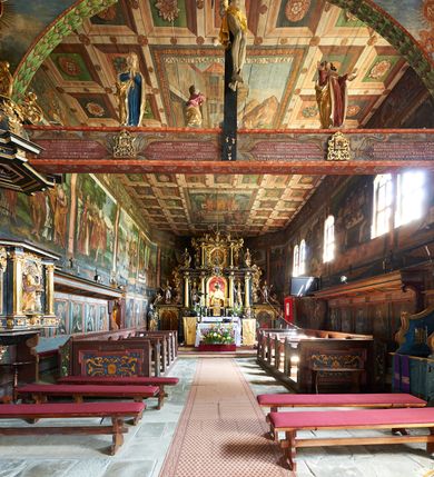 Zdjęcie nr 16: Kościół św. Jana Chrzciciela w Orawce usytuowany jest w centrum wsi na zachód od drogi prowadzącej z Jabłonki do Podwilka. Jest otoczony starodrzewiem, teren przykościelny opasany jest murem z łamanego kamienia. W granicach ogrodzenia znajduje się rozległy cmentarz przykościelny. 

Kościół orientowany, drewniany, konstrukcji zrębowej z wieżą na słup na kamiennej podmurówce. Prezbiterium wydłużone i zamknięte wielobocznie, nawa szersza i prostokątna. Przy prezbiterium od północy usytuowana jest zakrystia, a od wschodu murowana kaplica Matki Boskiej Bolesnej z 1728 roku o wielobocznym zakończeniu z przybudówką w rodzaju zakrystii od północy. Świątynia zbudowana jest z bierwion, łączonych na kwadratowy czop, bez ostatków. Poszczególne barwiona umocnione są pionowo tyblami. 

Wnętrze kościoła nakrywają stropy drewniane, płaskie, w nawie z zaskrzynieniami, podpartymi słupami. Zaskrzynienia w nawie obite są deskami dekorowanymi polichromią. W kaplicy Matki Boskiej Bolesnej sklepienie kolebkowe z lunetami. Ściana arkady tęczowej zamknięta jest łukiem półkolistym, na belce tęczowej umieszczona jest Grupa Ukrzyżowania. Przy nawie od południa dobudowana jest nowsza, drewniana kruchta. Chór muzyczny wsparty na dwóch profilowanych słupach z nim złączony chórek boczny przy północnej ścianie nawy. Otwory okienne usytuowane wyłącznie od strony południowej w kształcie stojących prostokątów, zamknięte półkoliście.

Na zewnątrz ściany świątyni obite gontem z wyjątkiem murowanej kaplicy Matki Boskiej Bolesnej, która została otynkowana. Wieża częściowo wtopiona w korpus, częściowo wysunięta ryzalitycznie; w przyziemiu babiniec. Wieża wzniesiona w konstrukcji słupowo-ramowej, główne narożne słupy nośne pochylone, wzmocnione tzw. krzyżami św. Andrzeja. Wieża zwieńczona jest nadwieszoną izbicą, szalowaną deskami w układzie pionowym z listwowaniem z czterolistnymi okienkami. Wyżej ostrosłupowy hełm z czterema narożnymi wieżyczkami. Kościół nakryty gontem w postaci długiego, kalenicowego dachu o rozległych połaciach, otulonym płaszczem gontowym z szerokim, załamanym okapem. Na wspólnym dachu kościoła i kaplicy nowa wieżyczka na sygnaturkę. 