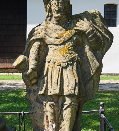 Zdjęcie nr 3: Kapliczka ustawiona na niskim prostopadłościennym postumencie. Pośrodku na wysokim cokole umieszczona kolumna, na której szczycie ustawiona jest figura Matki Boskiej Niepokalanie Poczętej z Dzieciątkiem. Cokół flankowany szerokimi spływami wolutowymi, na których ustawione są na niskich podstawach rzeźby: po lewej św. Donata, a po prawej św. Floriana. Na przedniej ściance cokołu znajduje się płaskorzeźba św. Marii Magdaleny ujęta płyciną w kształcie stojącego prostokąta, zamkniętego łukiem nadwieszonym z uskokami. Święta ukazana jest na tle groty, zwrócona trzy czwarte w prawo z rozpuszczonymi włosami, z dyscypliną w dłoni. Po lewej stronie kompozycji znajduje się wysoki, prosty krzyż i czaszka. Nad płyciną napis „ANNO D(OMI)NI 1758 / S(ANCTA) MARIA MAGDALENA / Zda SPPIPM”. Na tylnej ściance cokołu rzeźba św. Rozalii, ukazana w podobnym ujęciu z napisem „SANCTA ROSALIA VIRGO”. Święty Donat ukazany w postawie stojącej w delikatnym kontrapoście z księgą w lewej dłoni i trójzębem w prawej. Ubrany jest w strój biskupi: albę, komżę, kapę, infułę, rękawice i buty. Ma szeroką twarz, okoloną krótką brodą, bujne i długie włosy spływające na plecy. Na podstawie napis: „S(ANCTUS) DONATUS”. Po prawej stronie kolumny rzeźba św. Floriana, ustawionego frontalnie, który prawą ręką polewa wodą płonący dom, a lewą podtrzymuje u ramienia połę płaszcza. Ubrany jest w strój legionisty rzymskiego z hełmem o wyraźnie podkreślonym pióropuszu. Twarz szeroka, okolona średniej długości włosami, schowanymi pod hełmem. Podstawa pod rzeźbą opleciona metalowymi ściskami. Kolumna ustawiona na bazie, trzon gładki, dekorowany w połowie wysokości dwiema uskrzydlonymi główkami aniołów na tle promienistej glorii, kapitel koryncki. Rzeźba Matki Boskiej Niepokalanej z Dzieciątkiem na prawym ręku ustawiona jest frontalnie, w delikatnym kontrapoście na globie ziemskim, oplecionym przez węża. Maria ubrana jest w długą suknię i silnie drapowany płaszcz. Twarz owalna, okolona bujnymi i długimi włosami. Dzieciątko zwrócone jest w stronę Matki Boskiej. Rzeźba Marii osłonięta jest metalowym daszkiem wspartym na czterech prętach przytwierdzonych do metalowej opaski oplatającej kapitel kolumny. Kapliczka obwiedziona metalowym płotkiem. 

