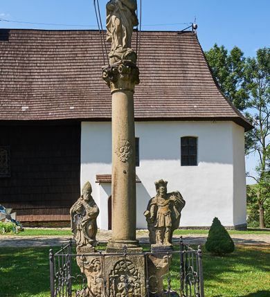 Zdjęcie nr 2: Kapliczka ustawiona na niskim prostopadłościennym postumencie. Pośrodku na wysokim cokole umieszczona kolumna, na której szczycie ustawiona jest figura Matki Boskiej Niepokalanie Poczętej z Dzieciątkiem. Cokół flankowany szerokimi spływami wolutowymi, na których ustawione są na niskich podstawach rzeźby: po lewej św. Donata, a po prawej św. Floriana. Na przedniej ściance cokołu znajduje się płaskorzeźba św. Marii Magdaleny ujęta płyciną w kształcie stojącego prostokąta, zamkniętego łukiem nadwieszonym z uskokami. Święta ukazana jest na tle groty, zwrócona trzy czwarte w prawo z rozpuszczonymi włosami, z dyscypliną w dłoni. Po lewej stronie kompozycji znajduje się wysoki, prosty krzyż i czaszka. Nad płyciną napis „ANNO D(OMI)NI 1758 / S(ANCTA) MARIA MAGDALENA / Zda SPPIPM”. Na tylnej ściance cokołu rzeźba św. Rozalii, ukazana w podobnym ujęciu z napisem „SANCTA ROSALIA VIRGO”. Święty Donat ukazany w postawie stojącej w delikatnym kontrapoście z księgą w lewej dłoni i trójzębem w prawej. Ubrany jest w strój biskupi: albę, komżę, kapę, infułę, rękawice i buty. Ma szeroką twarz, okoloną krótką brodą, bujne i długie włosy spływające na plecy. Na podstawie napis: „S(ANCTUS) DONATUS”. Po prawej stronie kolumny rzeźba św. Floriana, ustawionego frontalnie, który prawą ręką polewa wodą płonący dom, a lewą podtrzymuje u ramienia połę płaszcza. Ubrany jest w strój legionisty rzymskiego z hełmem o wyraźnie podkreślonym pióropuszu. Twarz szeroka, okolona średniej długości włosami, schowanymi pod hełmem. Podstawa pod rzeźbą opleciona metalowymi ściskami. Kolumna ustawiona na bazie, trzon gładki, dekorowany w połowie wysokości dwiema uskrzydlonymi główkami aniołów na tle promienistej glorii, kapitel koryncki. Rzeźba Matki Boskiej Niepokalanej z Dzieciątkiem na prawym ręku ustawiona jest frontalnie, w delikatnym kontrapoście na globie ziemskim, oplecionym przez węża. Maria ubrana jest w długą suknię i silnie drapowany płaszcz. Twarz owalna, okolona bujnymi i długimi włosami. Dzieciątko zwrócone jest w stronę Matki Boskiej. Rzeźba Marii osłonięta jest metalowym daszkiem wspartym na czterech prętach przytwierdzonych do metalowej opaski oplatającej kapitel kolumny. Kapliczka obwiedziona metalowym płotkiem. 

