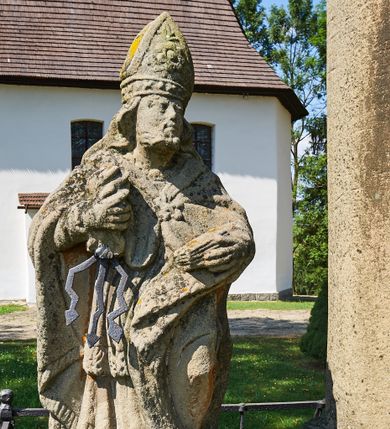 Zdjęcie nr 1: Kapliczka ustawiona na niskim prostopadłościennym postumencie. Pośrodku na wysokim cokole umieszczona kolumna, na której szczycie ustawiona jest figura Matki Boskiej Niepokalanie Poczętej z Dzieciątkiem. Cokół flankowany szerokimi spływami wolutowymi, na których ustawione są na niskich podstawach rzeźby: po lewej św. Donata, a po prawej św. Floriana. Na przedniej ściance cokołu znajduje się płaskorzeźba św. Marii Magdaleny ujęta płyciną w kształcie stojącego prostokąta, zamkniętego łukiem nadwieszonym z uskokami. Święta ukazana jest na tle groty, zwrócona trzy czwarte w prawo z rozpuszczonymi włosami, z dyscypliną w dłoni. Po lewej stronie kompozycji znajduje się wysoki, prosty krzyż i czaszka. Nad płyciną napis „ANNO D(OMI)NI 1758 / S(ANCTA) MARIA MAGDALENA / Zda SPPIPM”. Na tylnej ściance cokołu rzeźba św. Rozalii, ukazana w podobnym ujęciu z napisem „SANCTA ROSALIA VIRGO”. Święty Donat ukazany w postawie stojącej w delikatnym kontrapoście z księgą w lewej dłoni i trójzębem w prawej. Ubrany jest w strój biskupi: albę, komżę, kapę, infułę, rękawice i buty. Ma szeroką twarz, okoloną krótką brodą, bujne i długie włosy spływające na plecy. Na podstawie napis: „S(ANCTUS) DONATUS”. Po prawej stronie kolumny rzeźba św. Floriana, ustawionego frontalnie, który prawą ręką polewa wodą płonący dom, a lewą podtrzymuje u ramienia połę płaszcza. Ubrany jest w strój legionisty rzymskiego z hełmem o wyraźnie podkreślonym pióropuszu. Twarz szeroka, okolona średniej długości włosami, schowanymi pod hełmem. Podstawa pod rzeźbą opleciona metalowymi ściskami. Kolumna ustawiona na bazie, trzon gładki, dekorowany w połowie wysokości dwiema uskrzydlonymi główkami aniołów na tle promienistej glorii, kapitel koryncki. Rzeźba Matki Boskiej Niepokalanej z Dzieciątkiem na prawym ręku ustawiona jest frontalnie, w delikatnym kontrapoście na globie ziemskim, oplecionym przez węża. Maria ubrana jest w długą suknię i silnie drapowany płaszcz. Twarz owalna, okolona bujnymi i długimi włosami. Dzieciątko zwrócone jest w stronę Matki Boskiej. Rzeźba Marii osłonięta jest metalowym daszkiem wspartym na czterech prętach przytwierdzonych do metalowej opaski oplatającej kapitel kolumny. Kapliczka obwiedziona metalowym płotkiem. 

